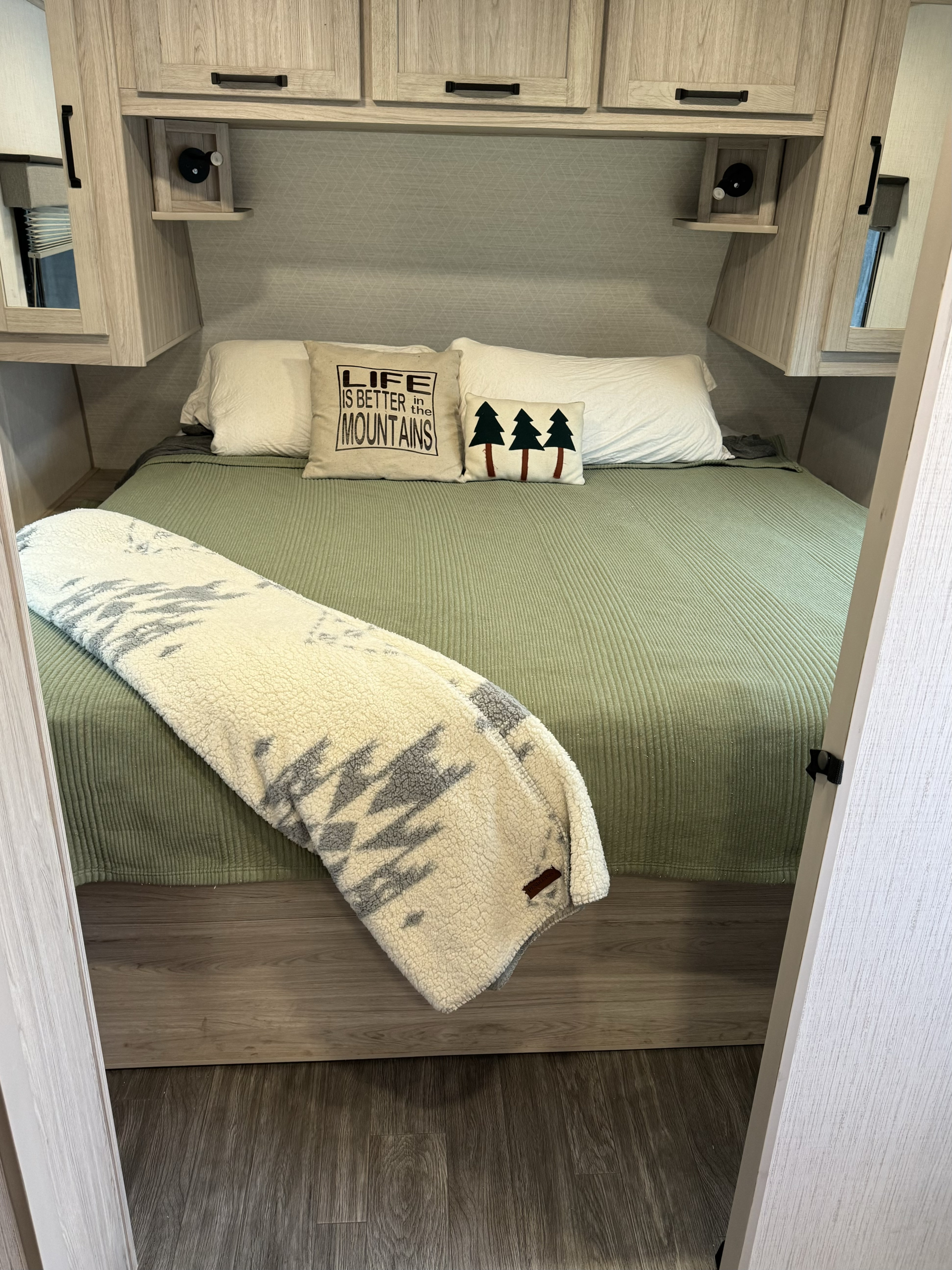 Cozy RV rental bedroom with a comfy bed, green comforter, mountain pillows, and light wood cabinetry.. Cruiser Twighlight Signature 2023