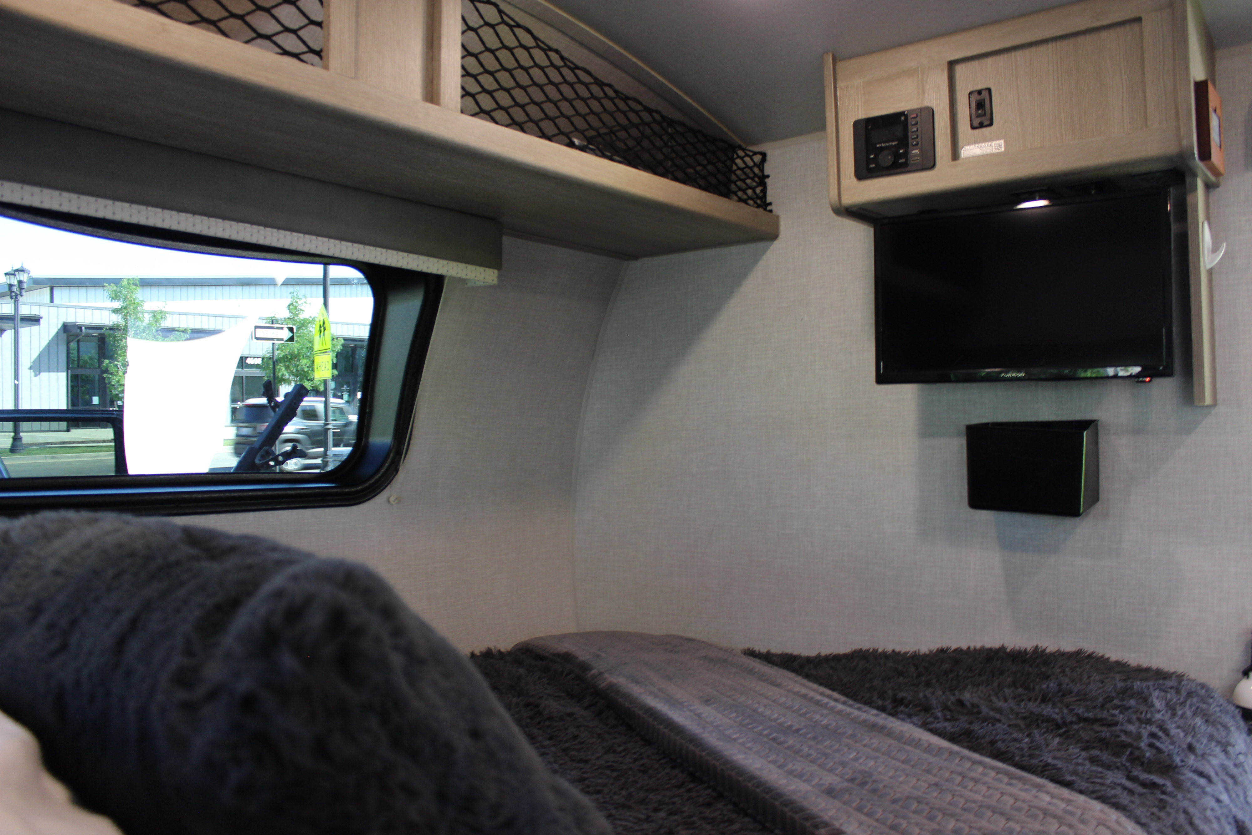 RV rental bedroom interior with TV, overhead storage net, and a window overlooking a street scene.. Forest River GeoPro 2021