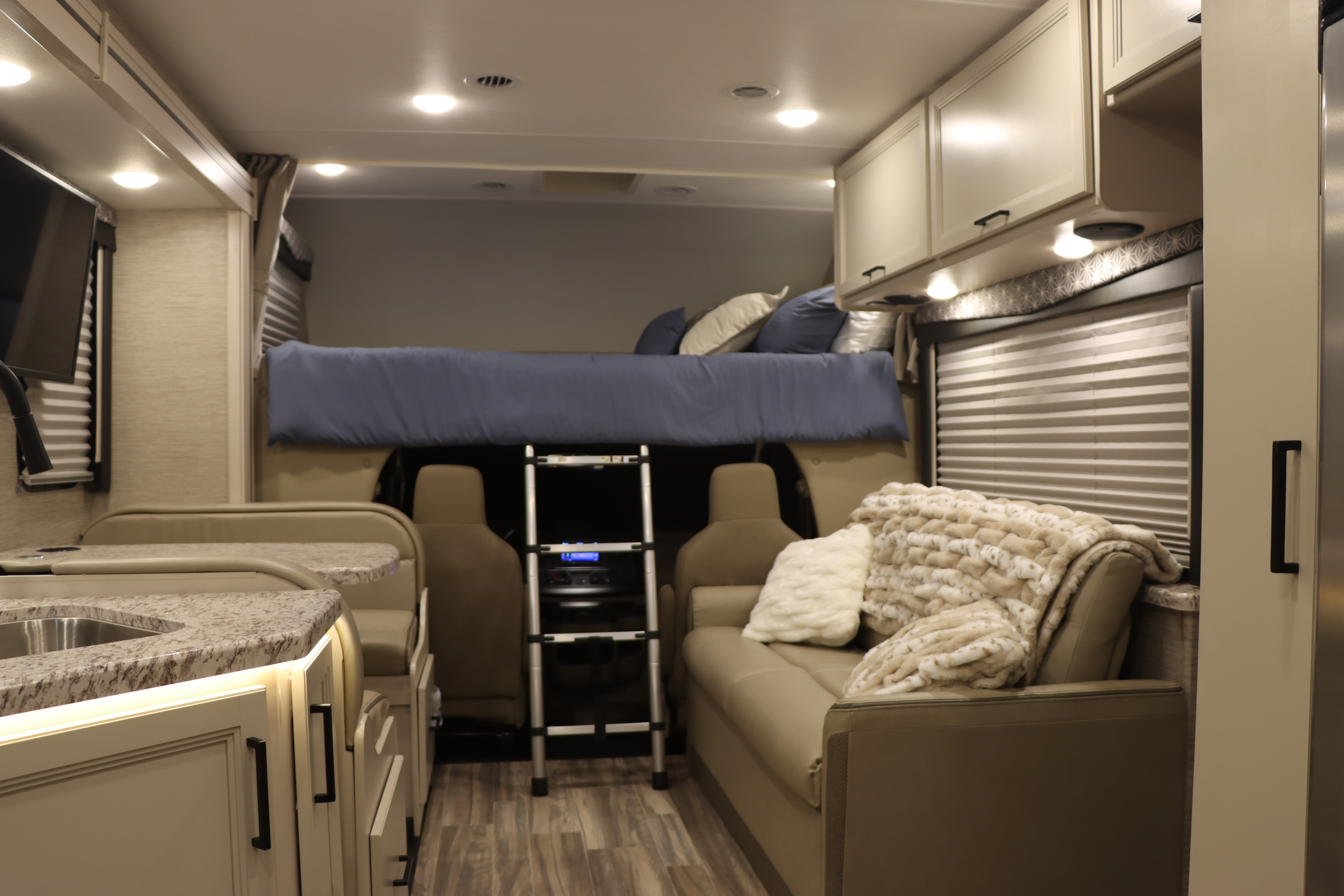 Comfortable RV rental interior showing kitchen, dinette, living area with sofa, and overhead bunk bed with ladder.. Thor Freedom Elite 2023