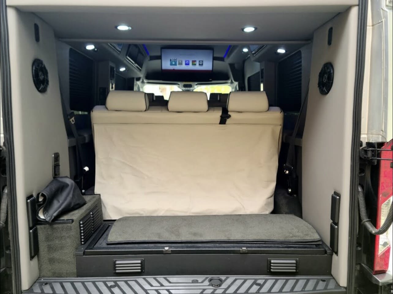 Spacious RV rental van interior featuring a comfortable rear bench, overhead TV, and built-in storage.. Ford Transit Custom 2017