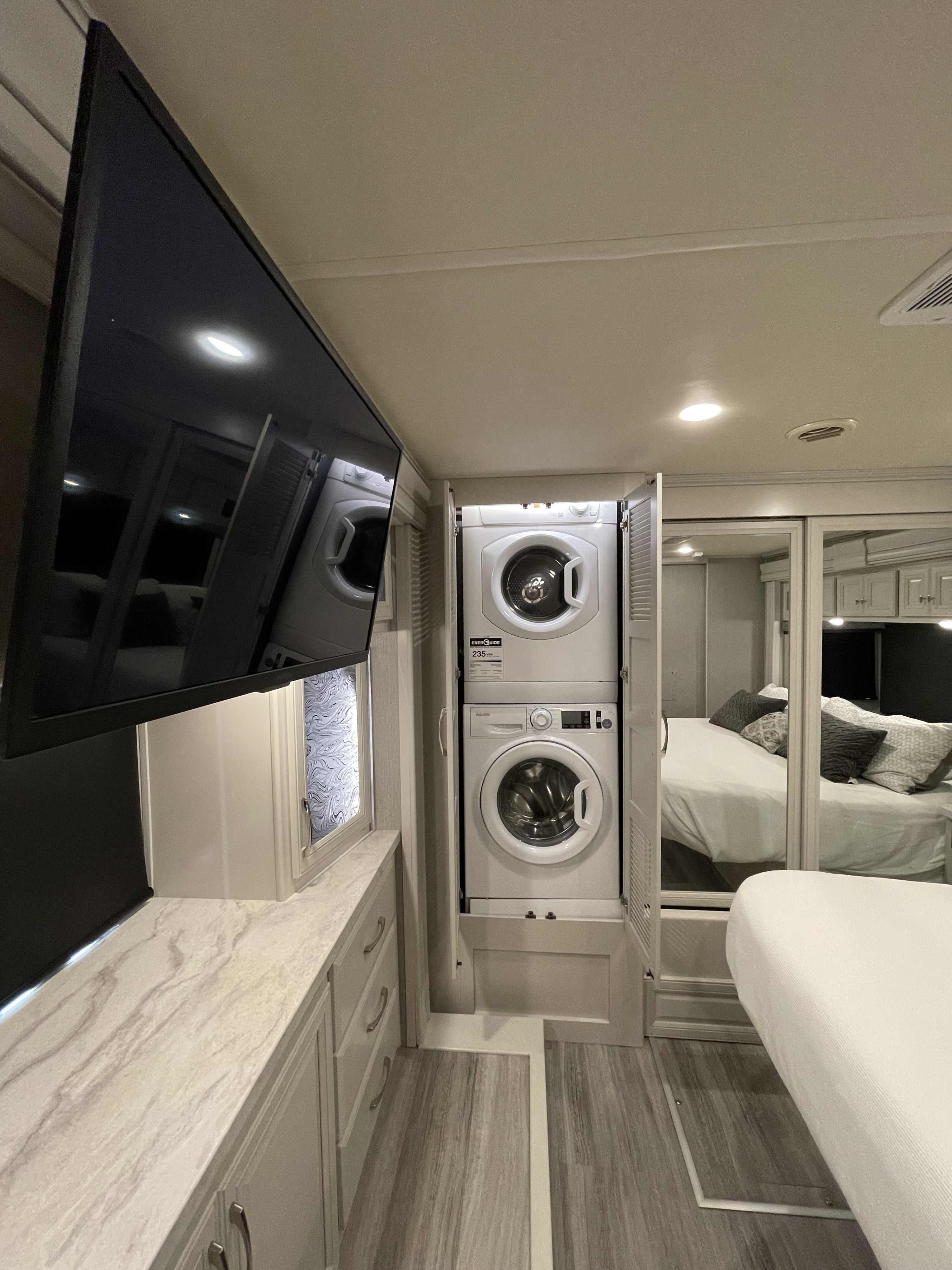 Luxury RV rental interior with practical amenities: large TV, stacked washer/dryer unit, and a cozy bedroom area.. Holiday Rambler Nautica 2021