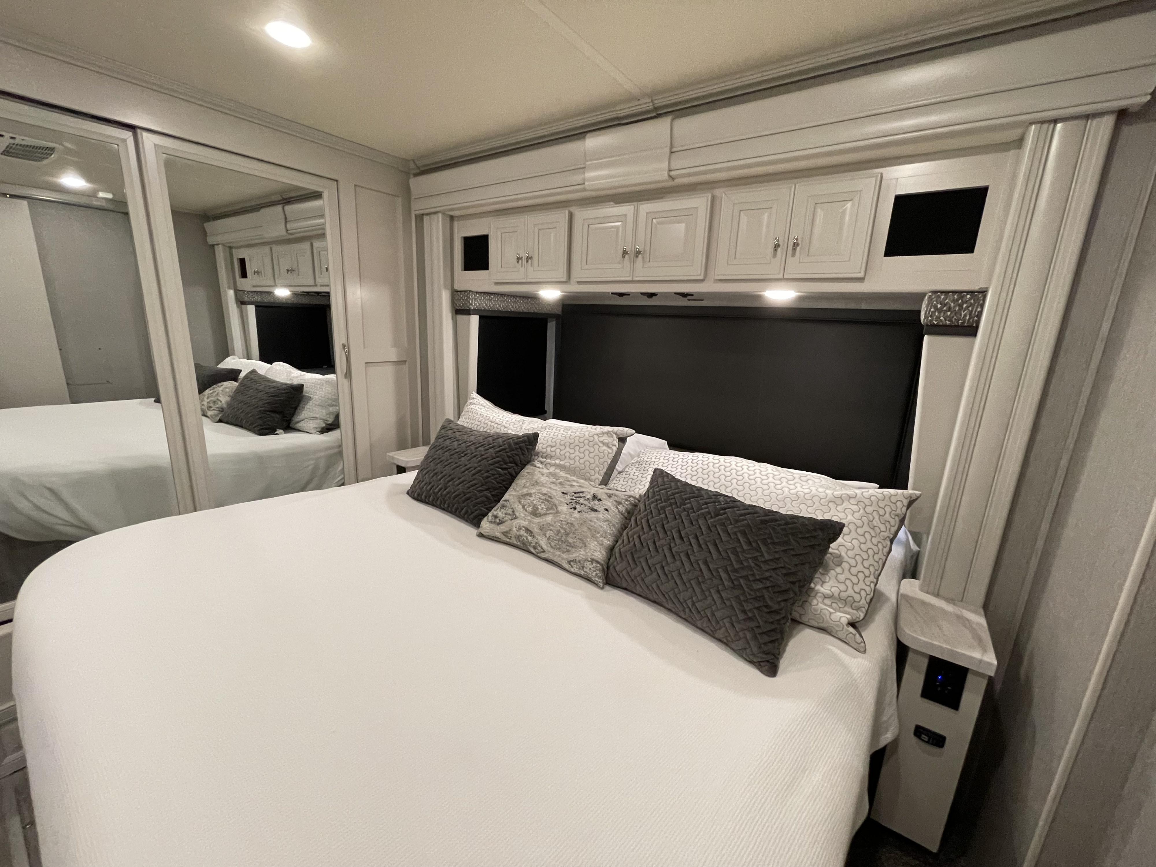 Bright RV rental bedroom with a large bed, mirrored closet, extensive overhead storage, and bedside charging station.. Holiday Rambler Nautica 2021