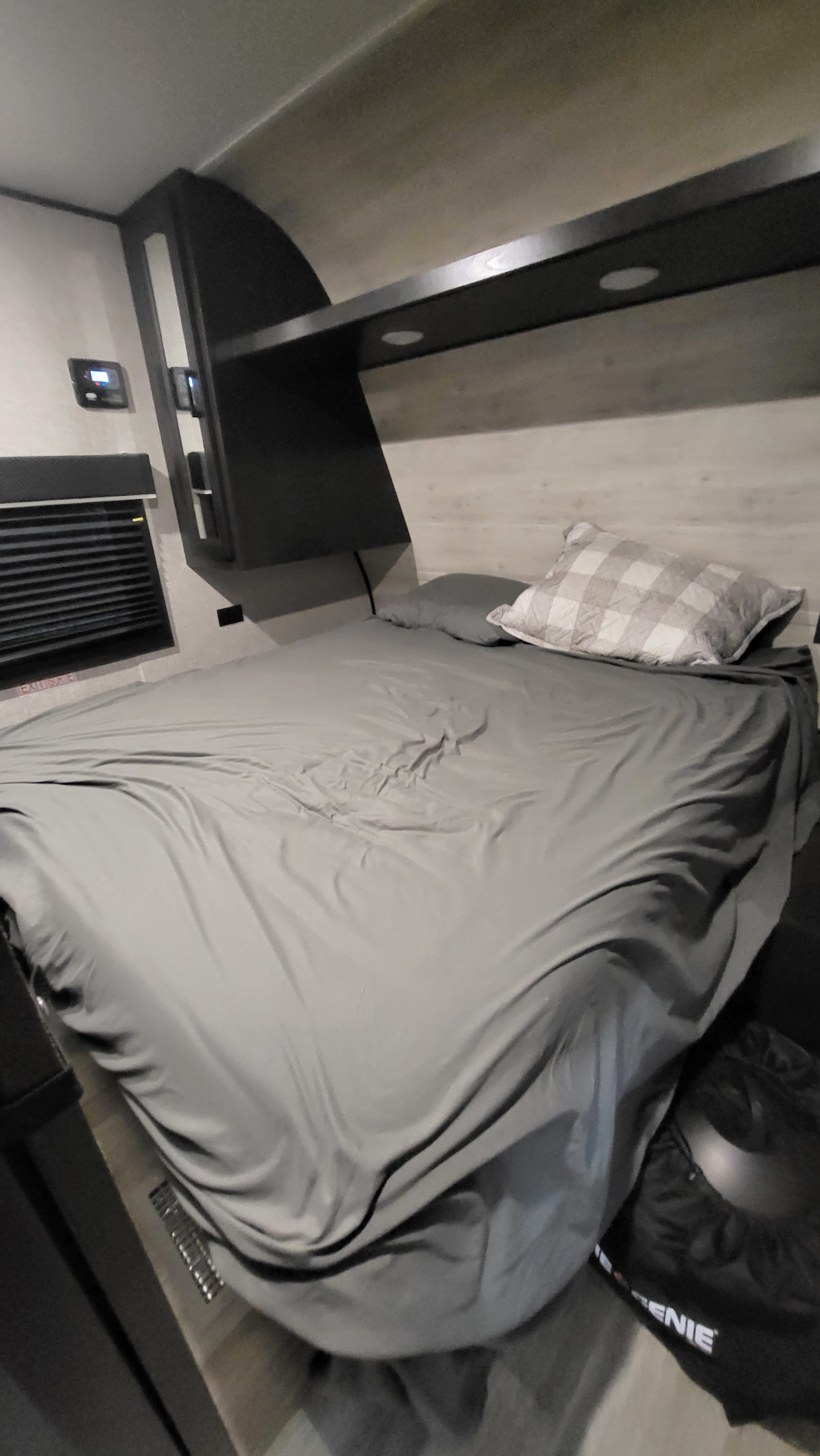 Inside an RV rental: a modern, compact bedroom with a gray bed, plaid pillow, overhead shelf with lights, and controls.. Jayco Jay Flight SLX Rocky Mountain Edition 2022
