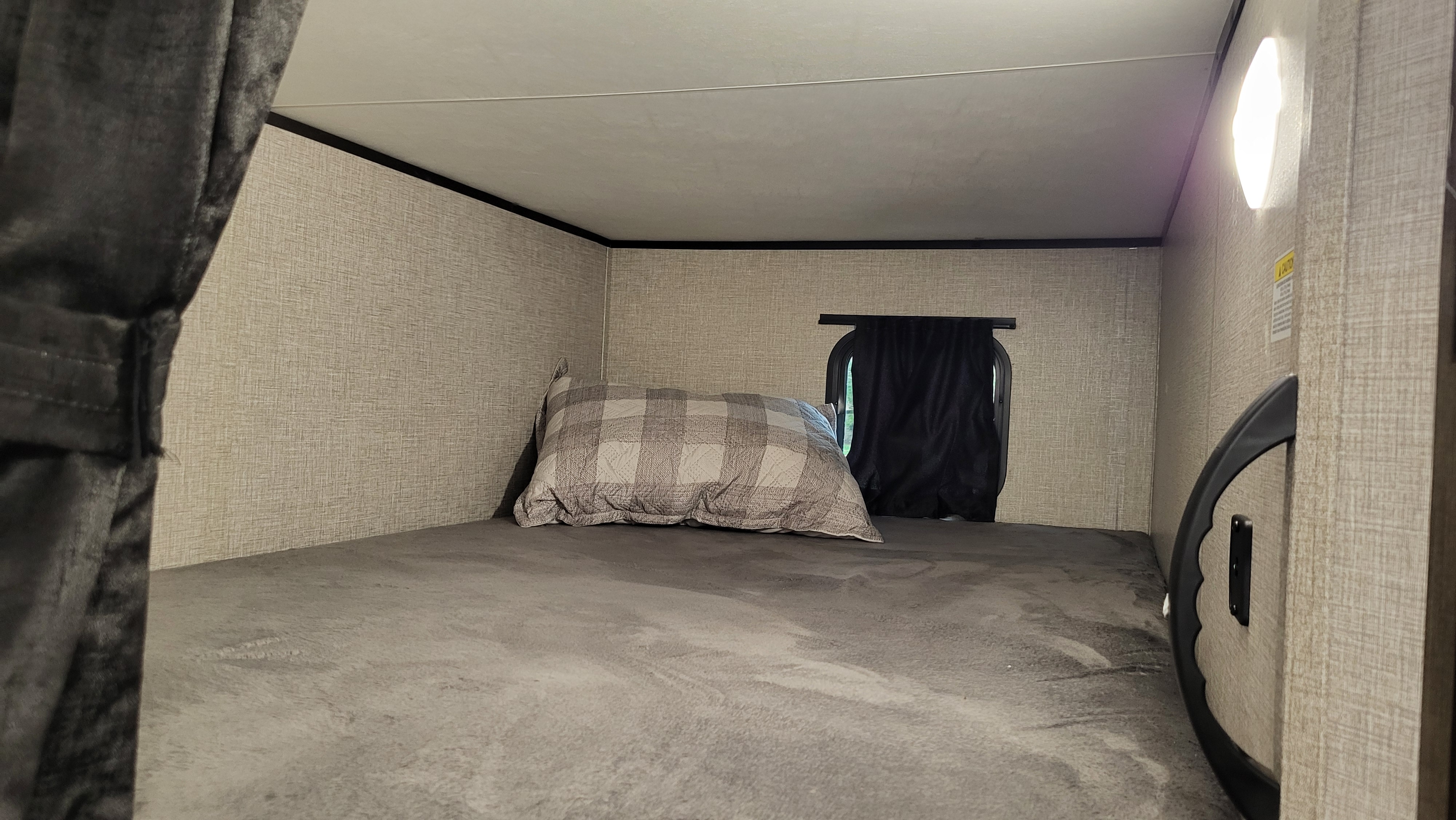 Inside an RV rental bunk bed: gray bedding, plaid pillow, window with curtain, and wall light. A cozy sleeping space.. Jayco Jay Flight SLX Rocky Mountain Edition 2022