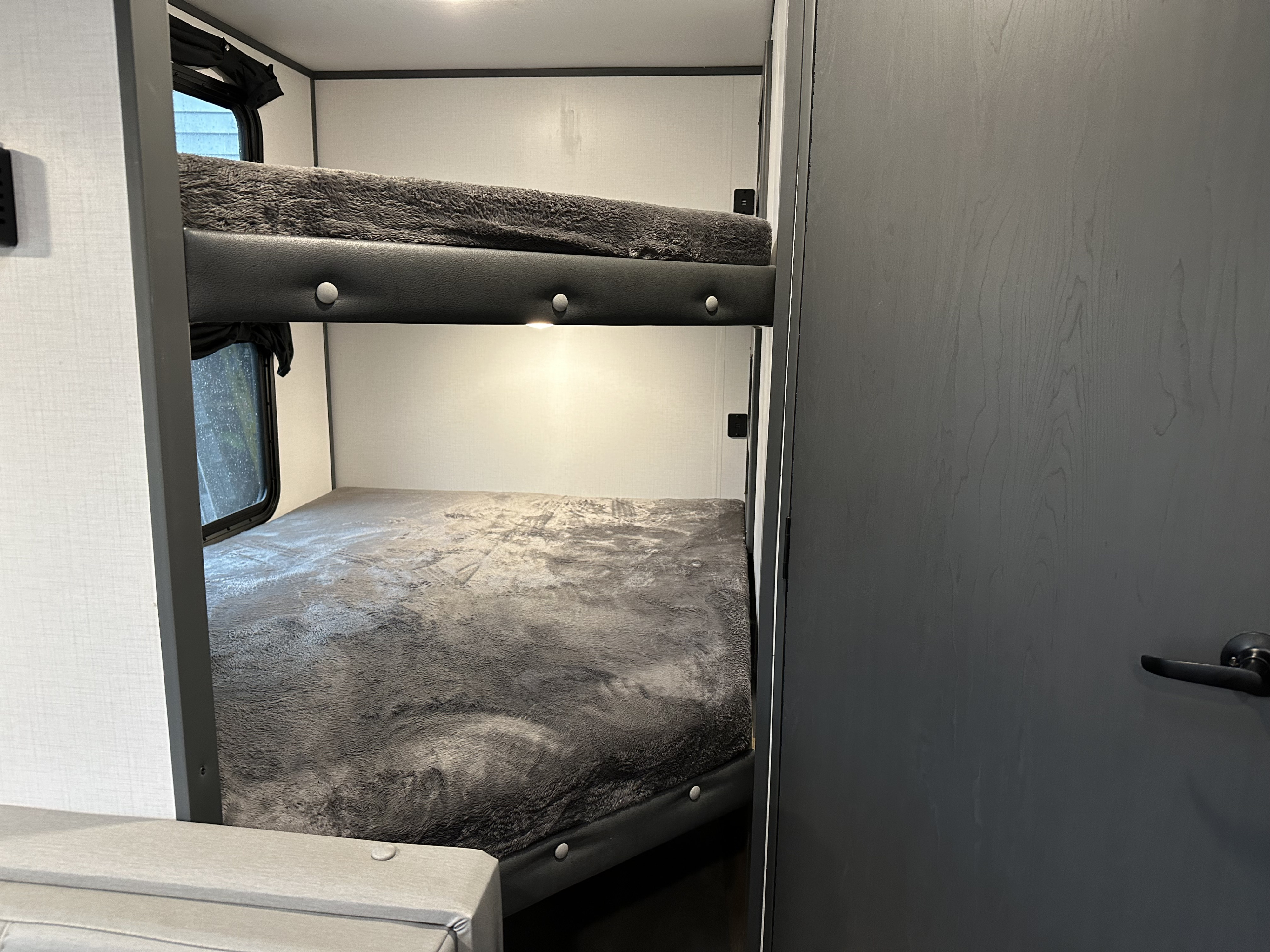 Interior view of an RV rental showing modern bunk beds with soft grey blankets. Ideal for comfortable travel and camping adventures.. Keystone RV Bullet Crossfire 2022
