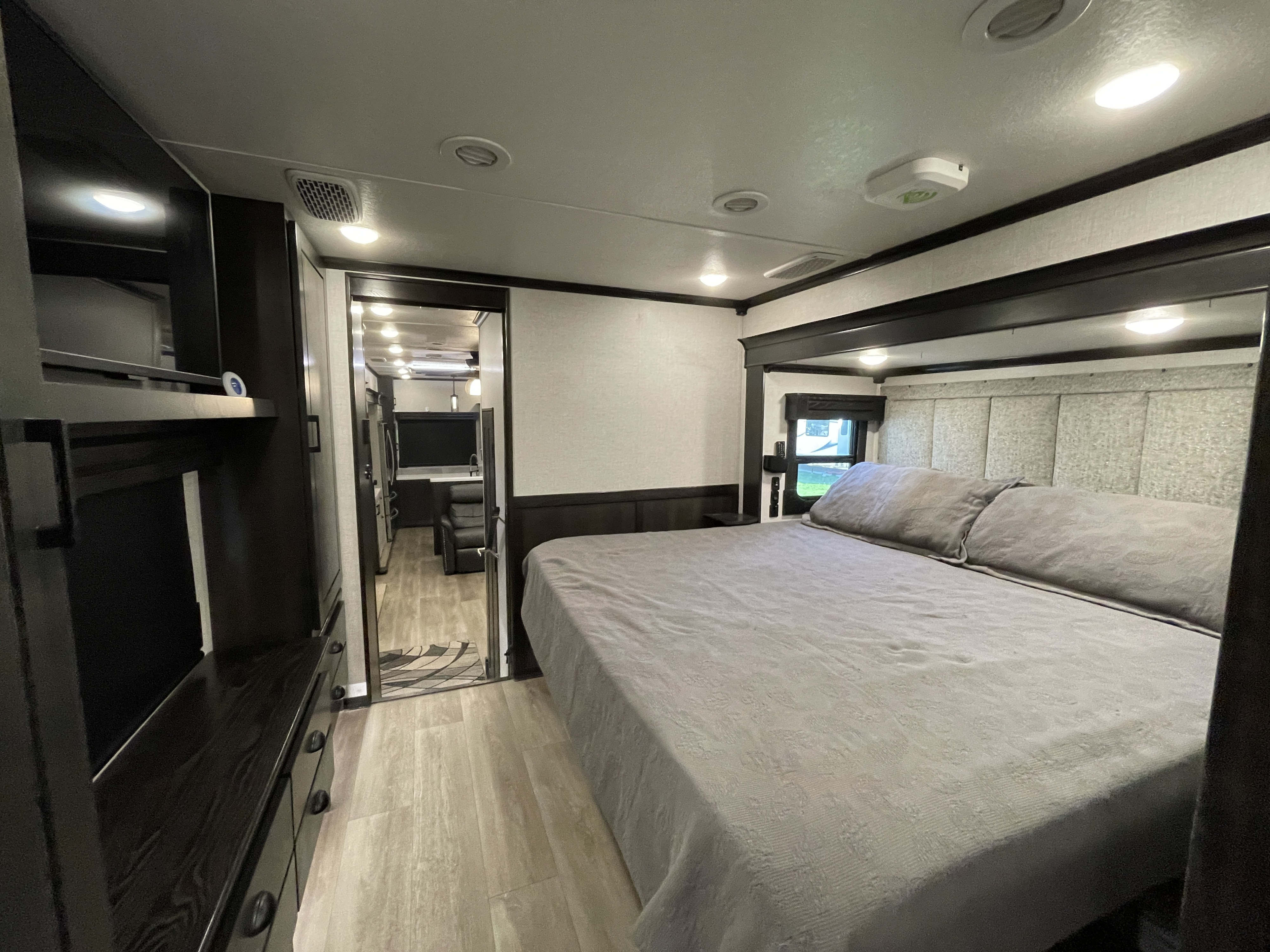 Comfortable RV rental bedroom with a large bed, dark wood furniture, and doorway leading to the RV's main living area.. Crossroads Redwood 2021