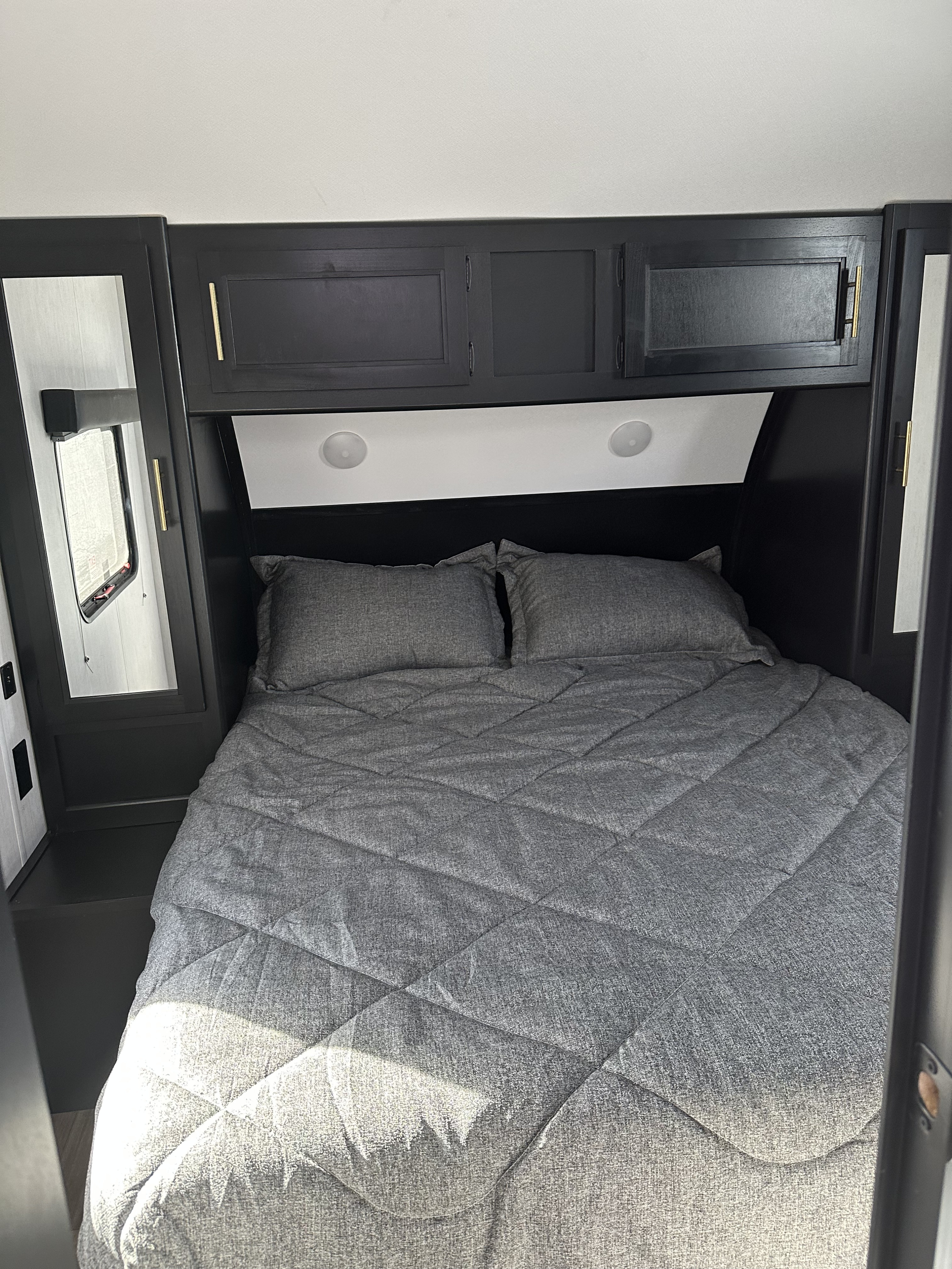 Experience comfort in this RV rental bedroom with dark wood cabinets, grey quilted bedding, and integrated lighting.. Forest River Cherokee Grey Wolf 2023