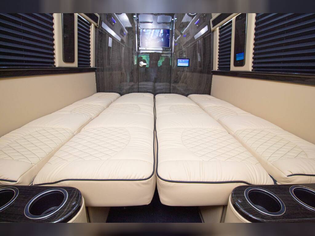 Two rows of plush cream beds with quilted patterns and cup holders line this luxurious RV rental interior, ready for travel.. Mercedes-Benz Benz 2022