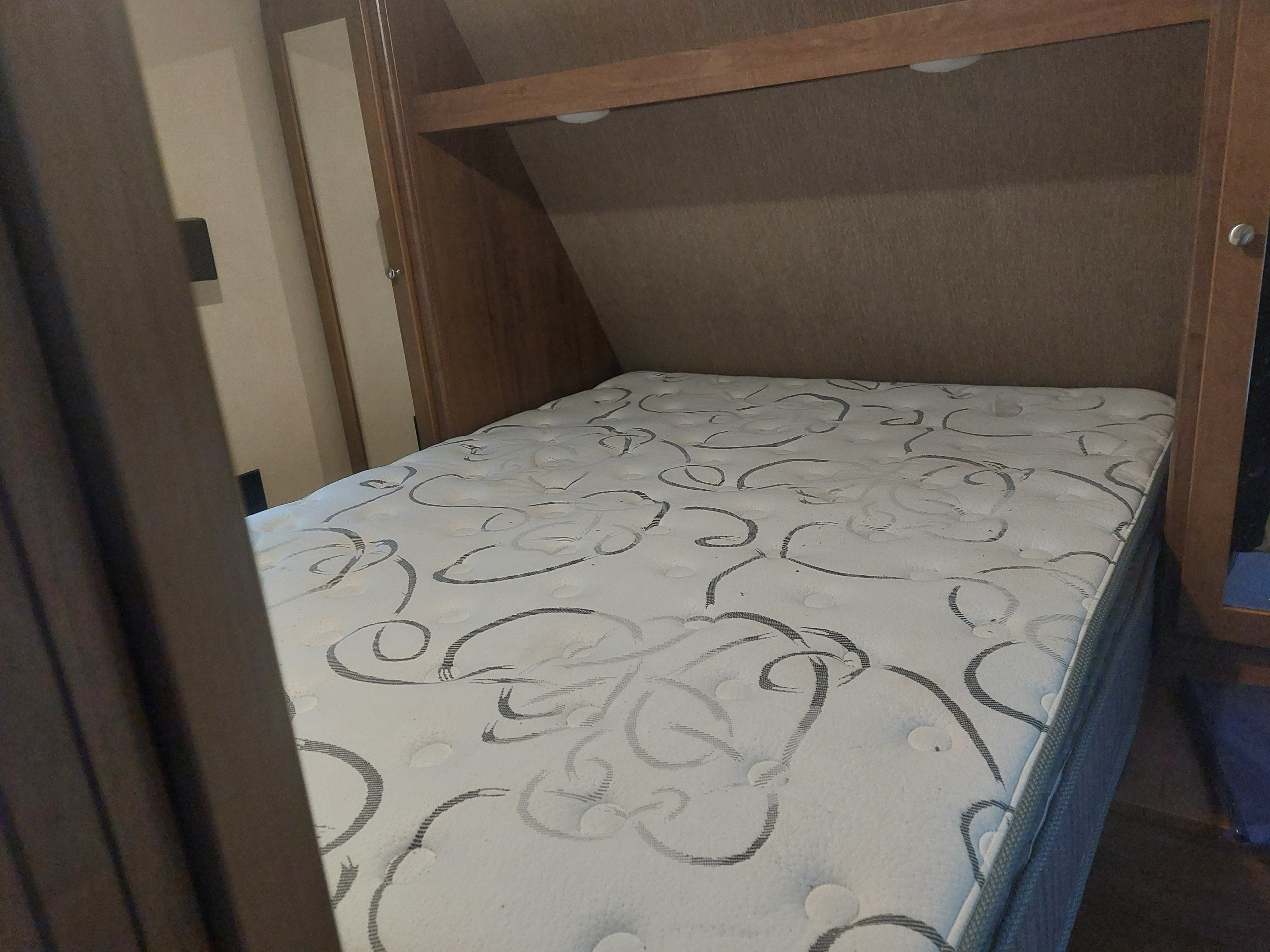 An RV rental bedroom with a white patterned mattress, built-in wooden shelving, and compact interior space.. Aspen 3010 2017