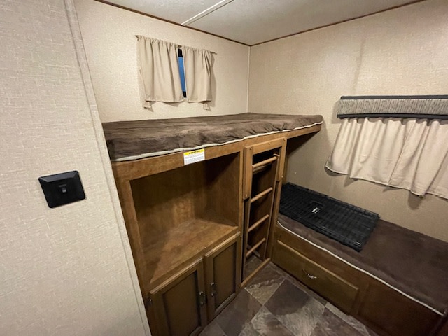 Cozy RV rental bunk room: upper bed with ladder, lower bed/bench, and wooden storage cabinets. Ideal for family adventures.. Crossroads RV Rezerve 2017