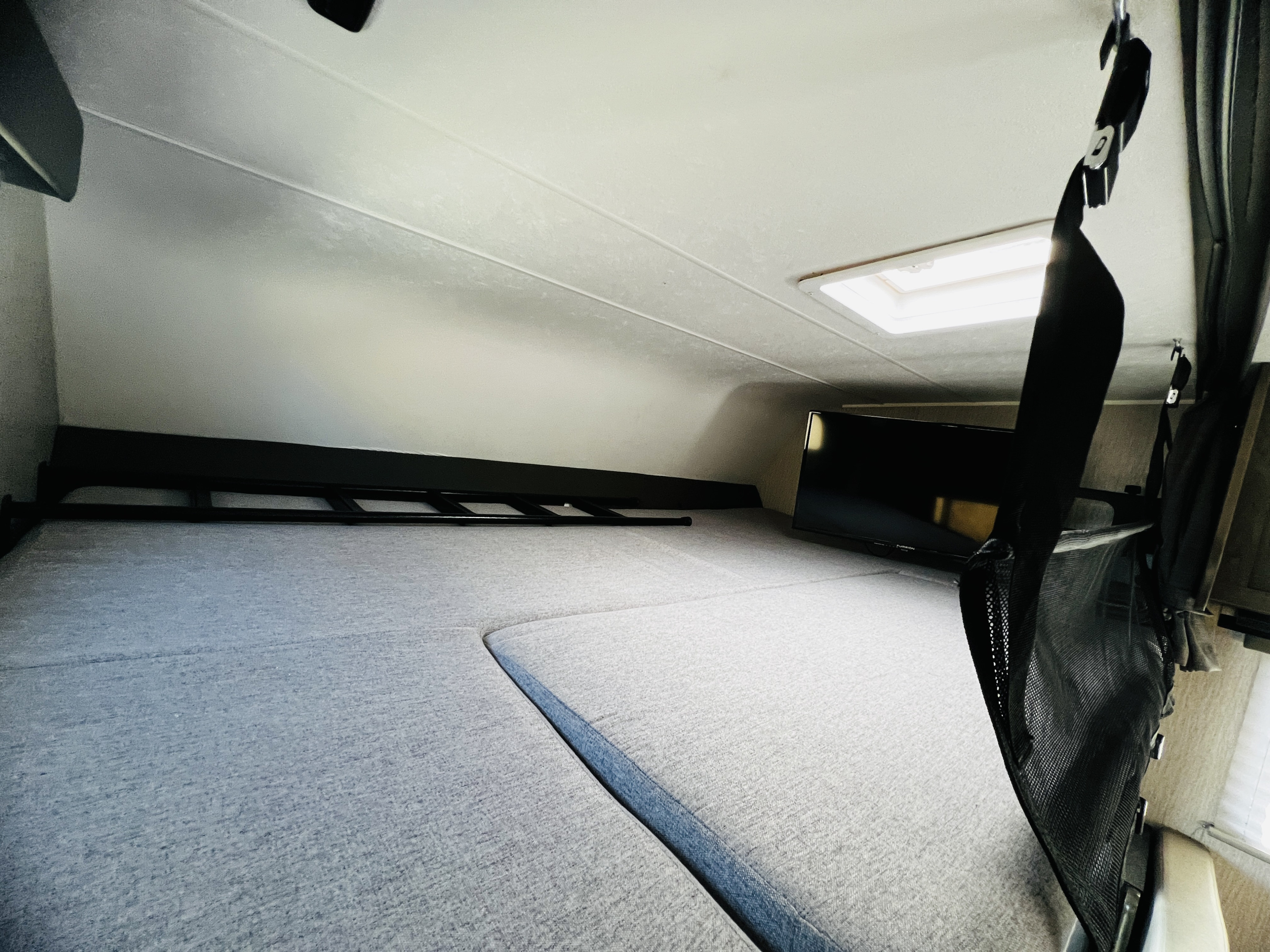 This RV rental's over-cab bunk features a TV, ladder, and plush cushions, perfect for sleeping or lounging on your trip.. Forest River Coachmen Leprechaun 2023