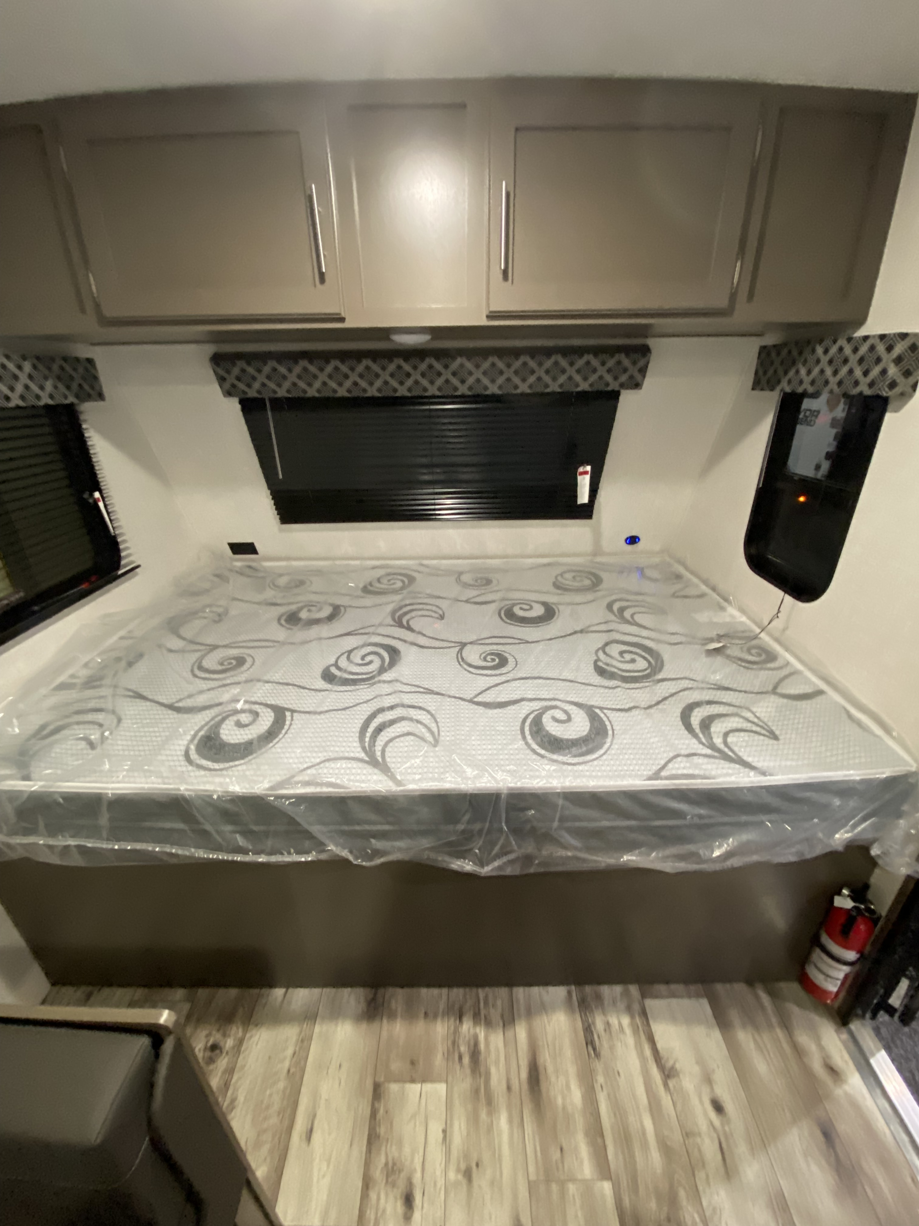 Clean RV rental bedroom with a new bed in plastic, overhead storage, and windows.. KZ Sportsmen Classic 180BH 2024