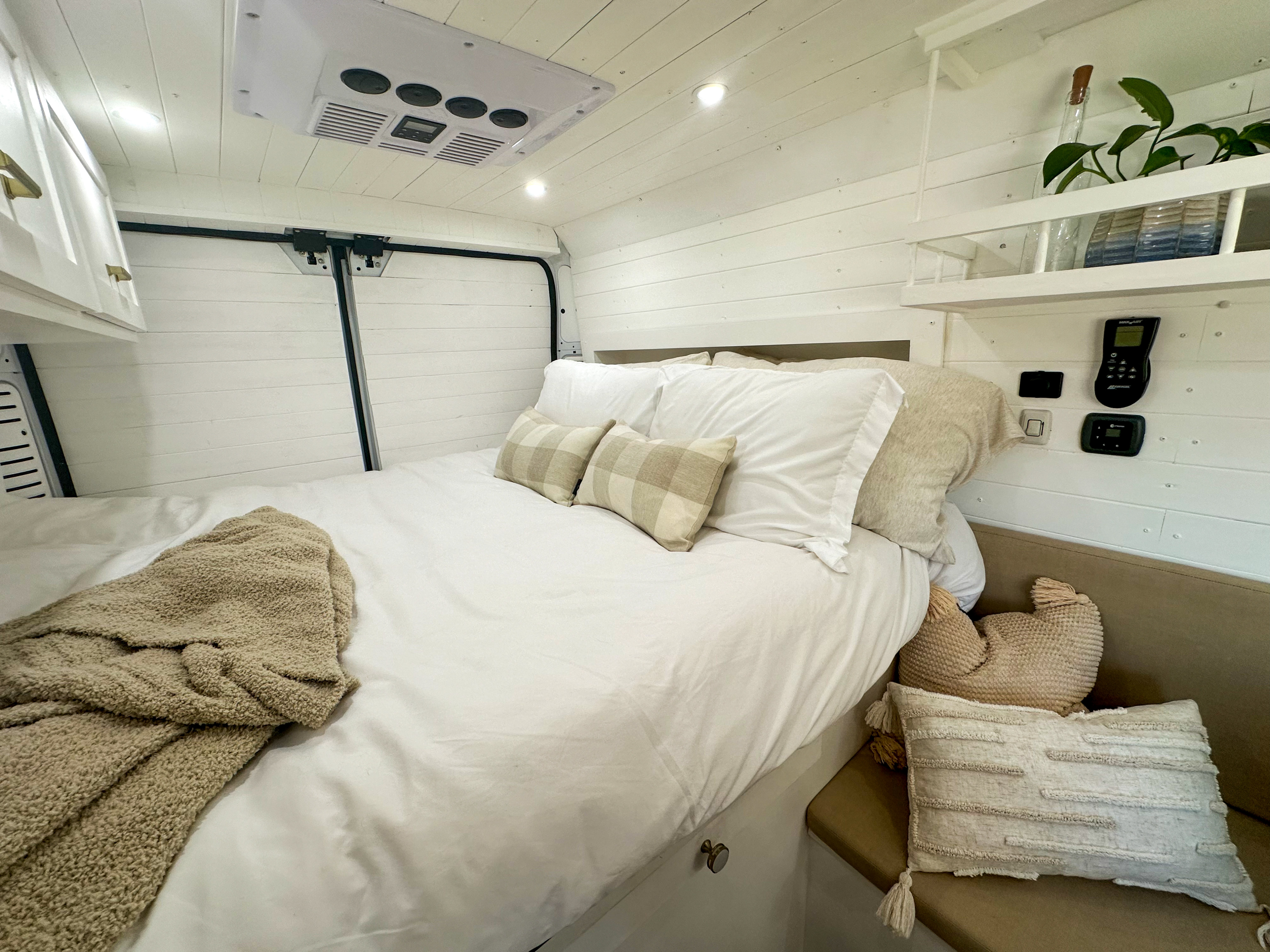 RV rental interior: A bright bedroom with white shiplap walls, soft bedding, built-in shelf, and controls.. Dodge Promaster 3500 2021