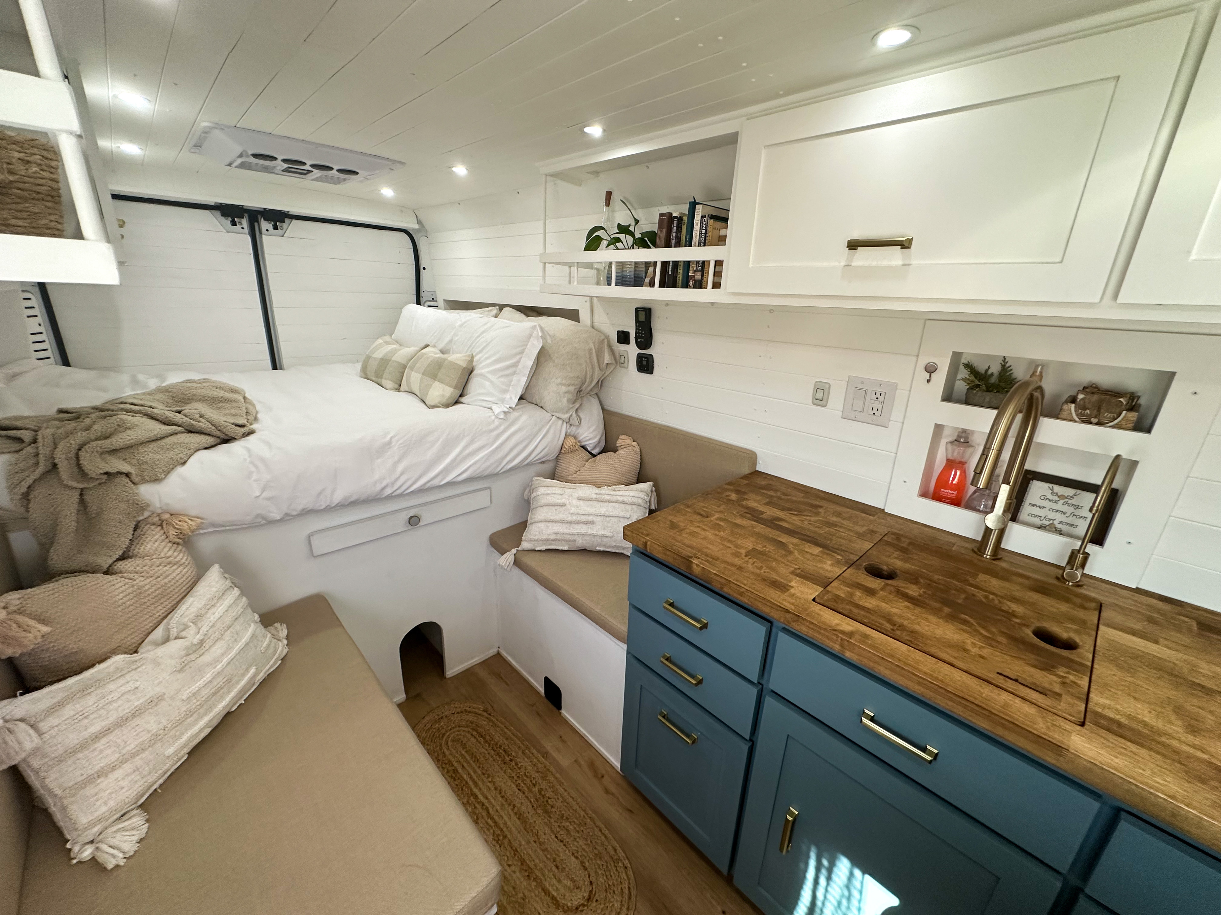 Bright rv rental interior featuring a bed, kitchenette with wooden counter and blue cabinets, plus cozy seating for mobile living.. Dodge Promaster 3500 2021