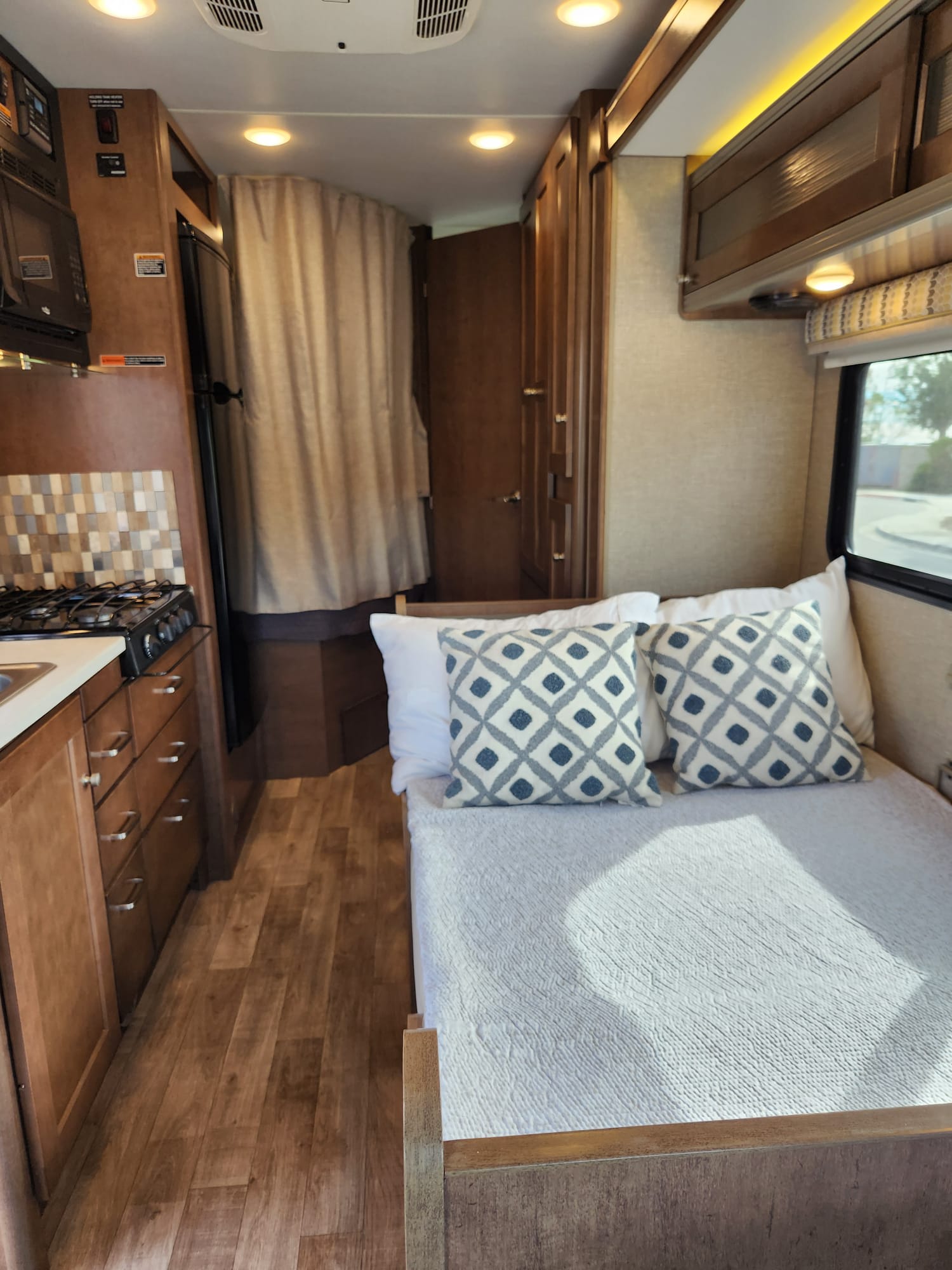 RV rental interior: modern kitchen, wooden cabinets, and a comfortable bed. A cozy, well-lit mobile living space awaits.. Winnebago Fuse 2019