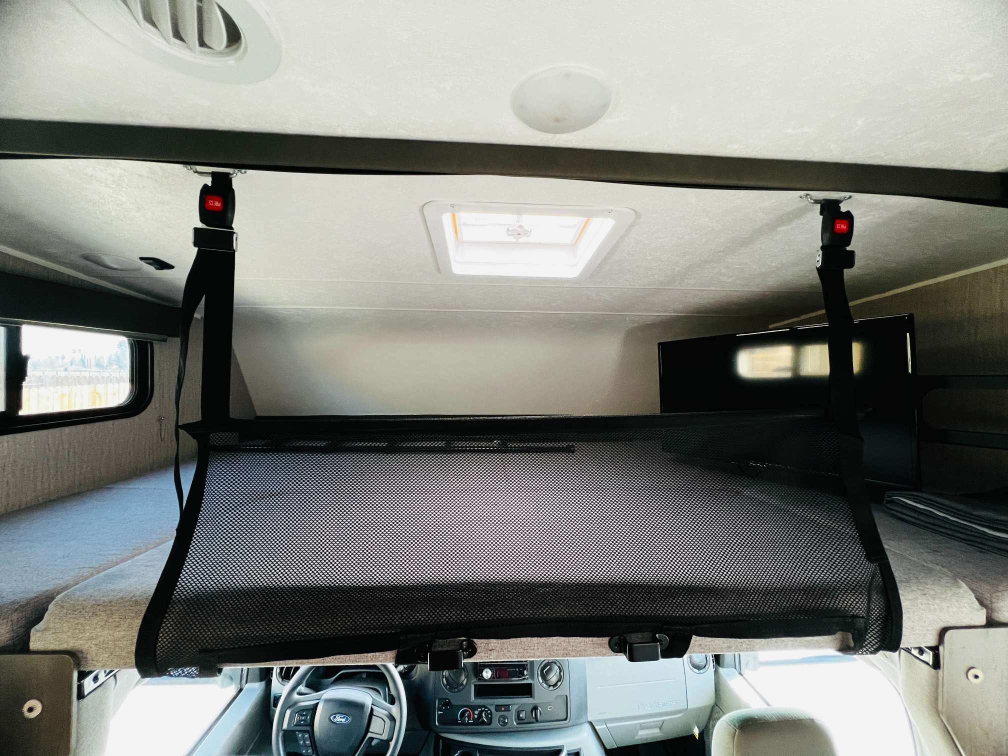 RV rental's cab-over bunk with a safety net deployed. Includes a view of the Ford steering wheel & dash.. Forest River Coachmen Leprechaun 2023