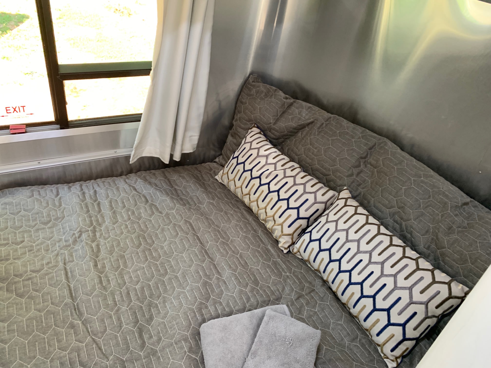 Cozy RV rental sleeping area features quilted grey bedding, geometric pillows, and an exit window.. Airstream Sport 2019
