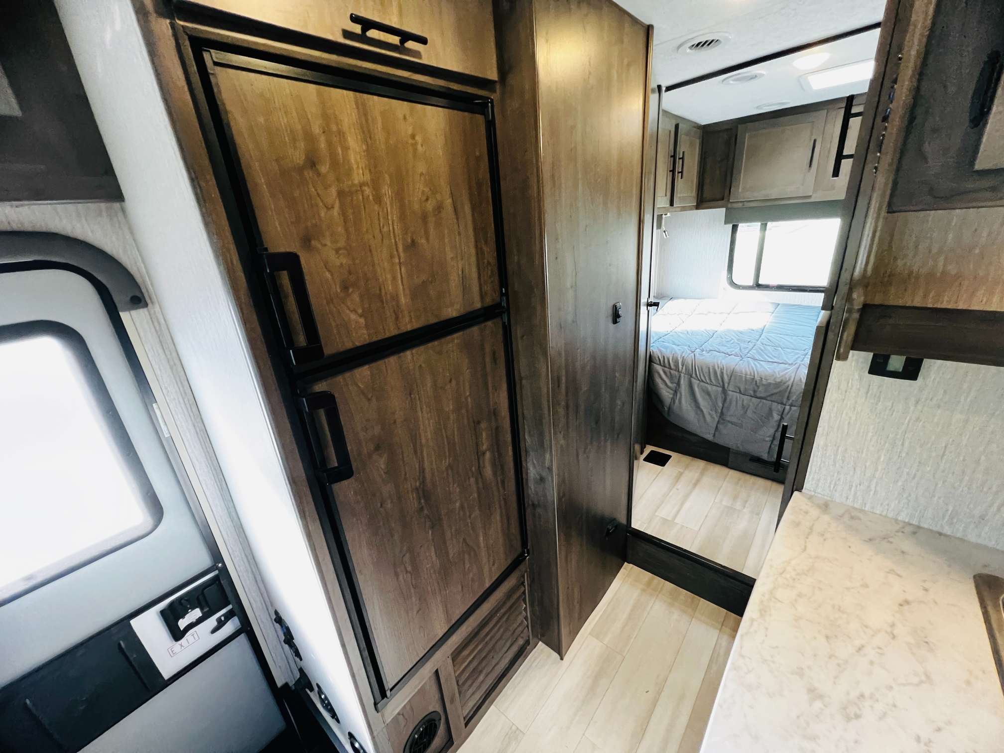 This RV rental interior showcases a wood-paneled refrigerator, adjacent private bedroom with a bed, and efficient living areas.. Forest River Coachmen Leprechaun 2023