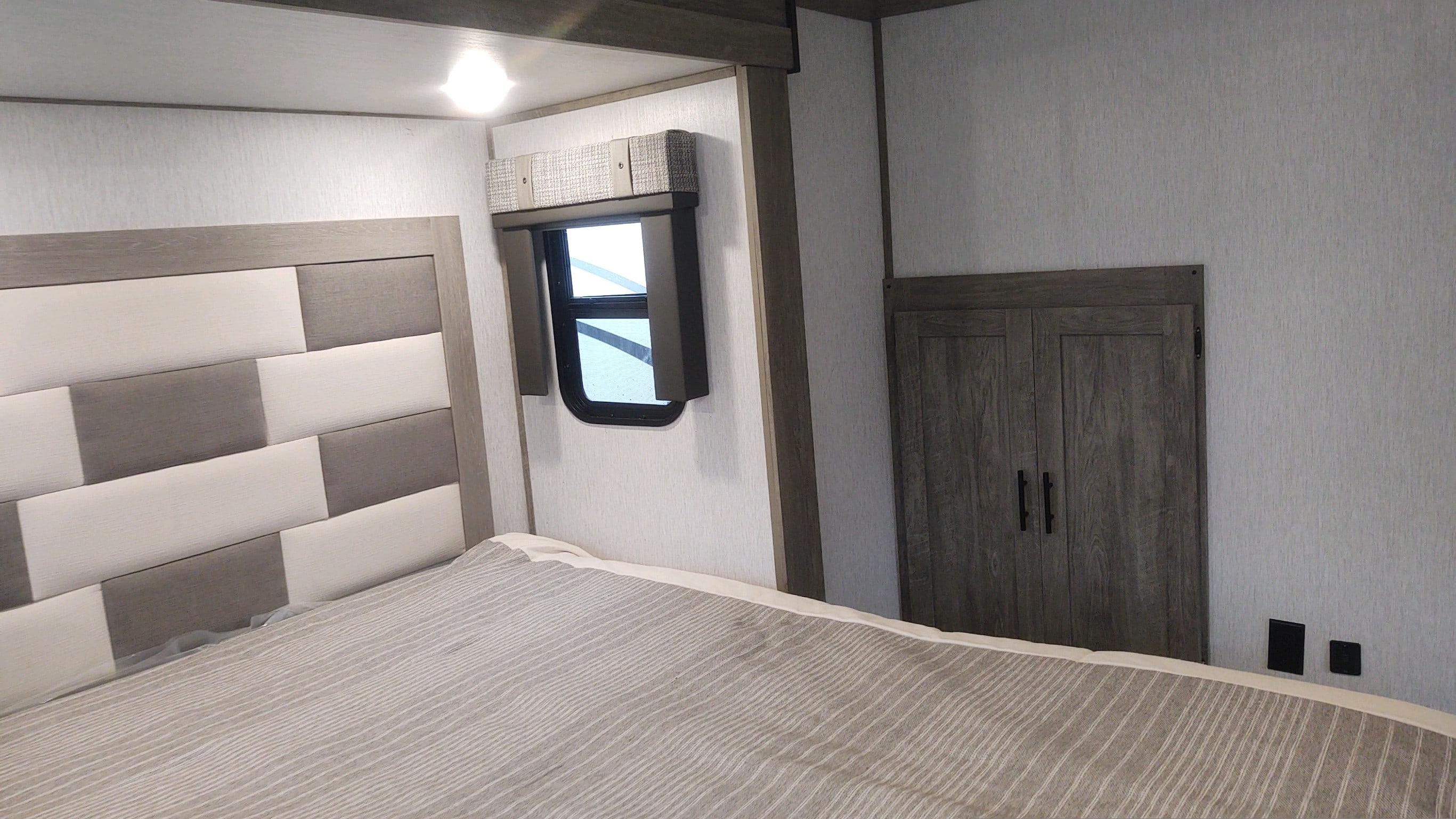 Cozy RV rental bedroom: bed with striped bedding, gray/white upholstered headboard, window, and wood closet.. Forest River Salem Hemisphere 2022