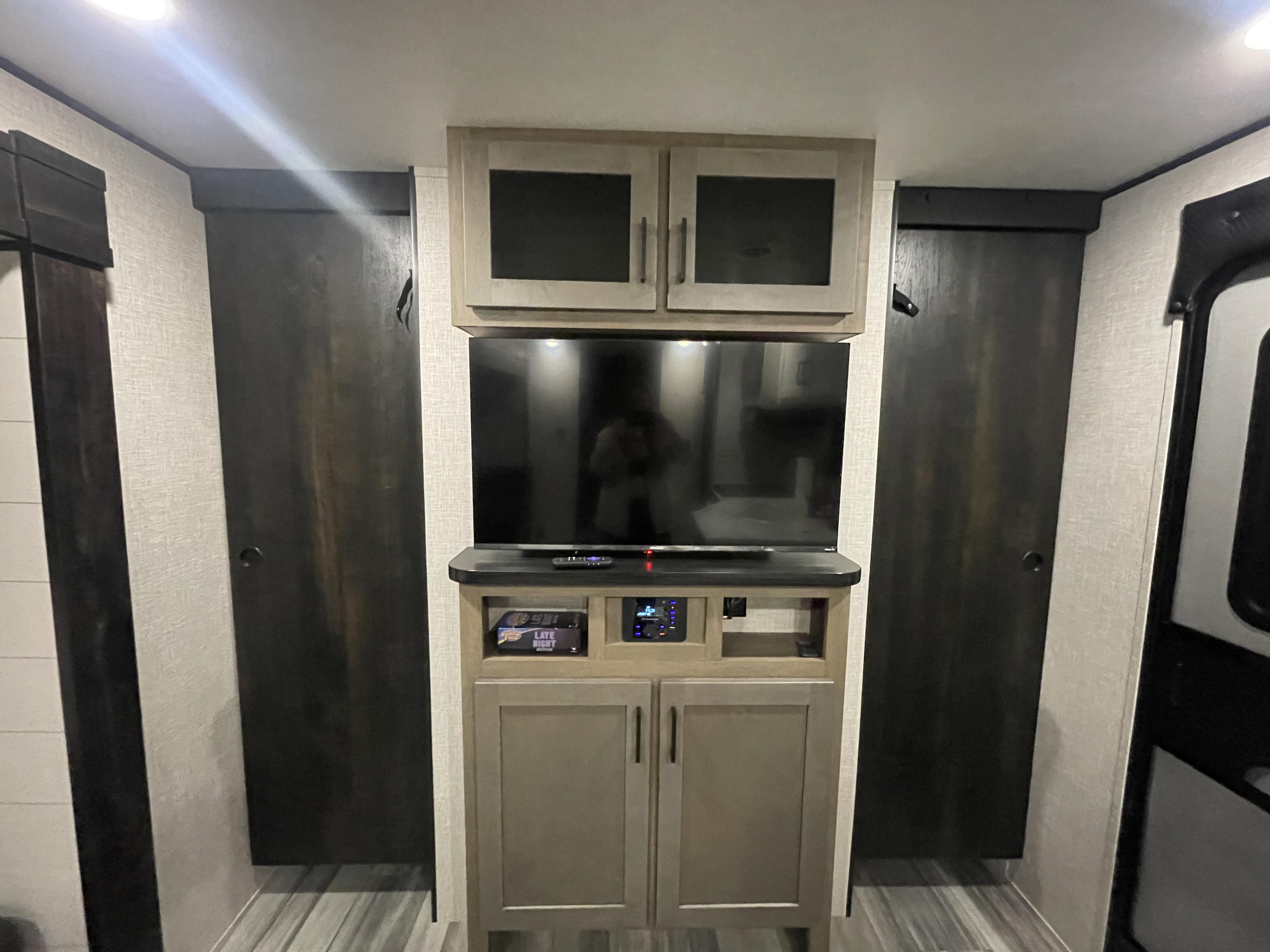 RV rental interior: A central entertainment setup with TV, media system, and various cabinets. Flanked by dark wardrobe doors.. Jayco Jay Flight 261BHS 2024