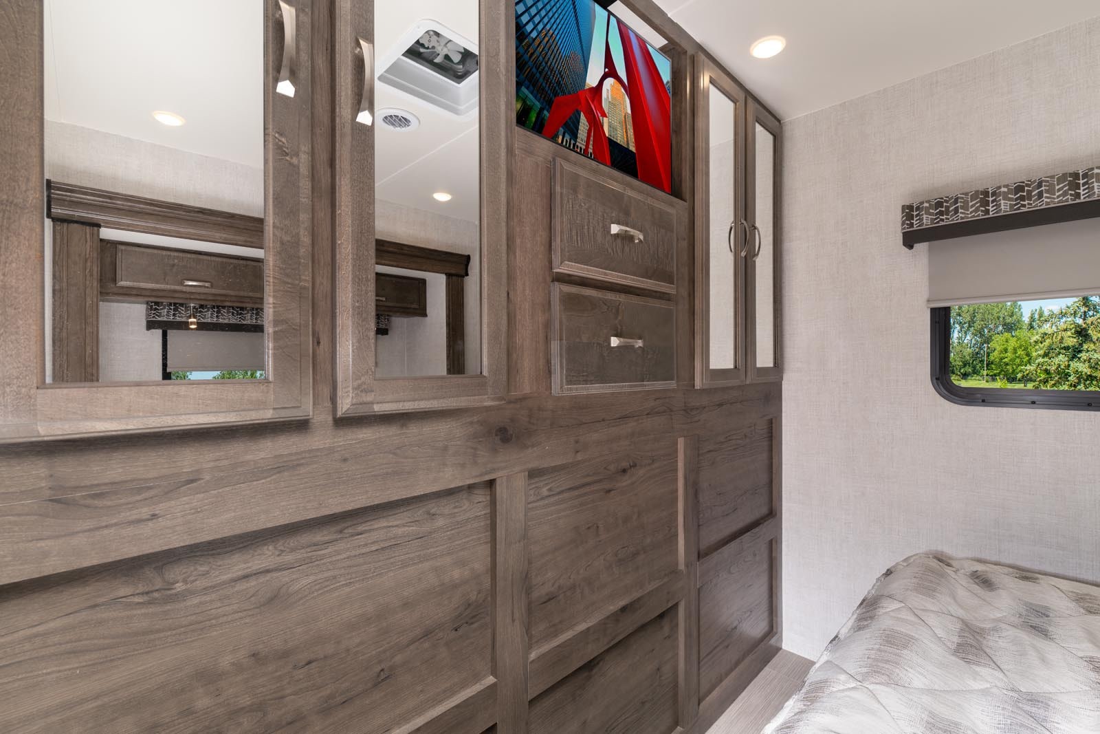 RV rental bedroom with wood-grain cabinets, built-in TV, mirrored doors, and a scenic window view.. CONQUEST 6320D 2024