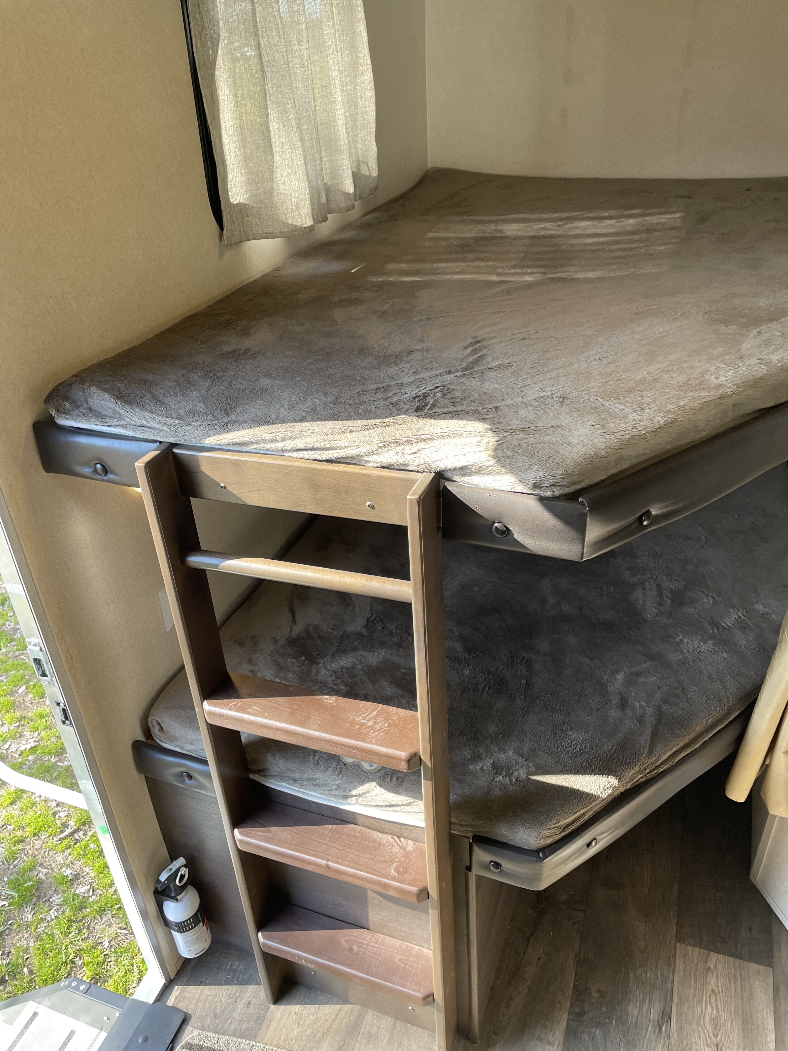 Inside an RV rental, two bunk beds with fuzzy mattresses and a ladder are illuminated by sunlight. A fire extinguisher is mounted nearby.. Forest River Salem 2018