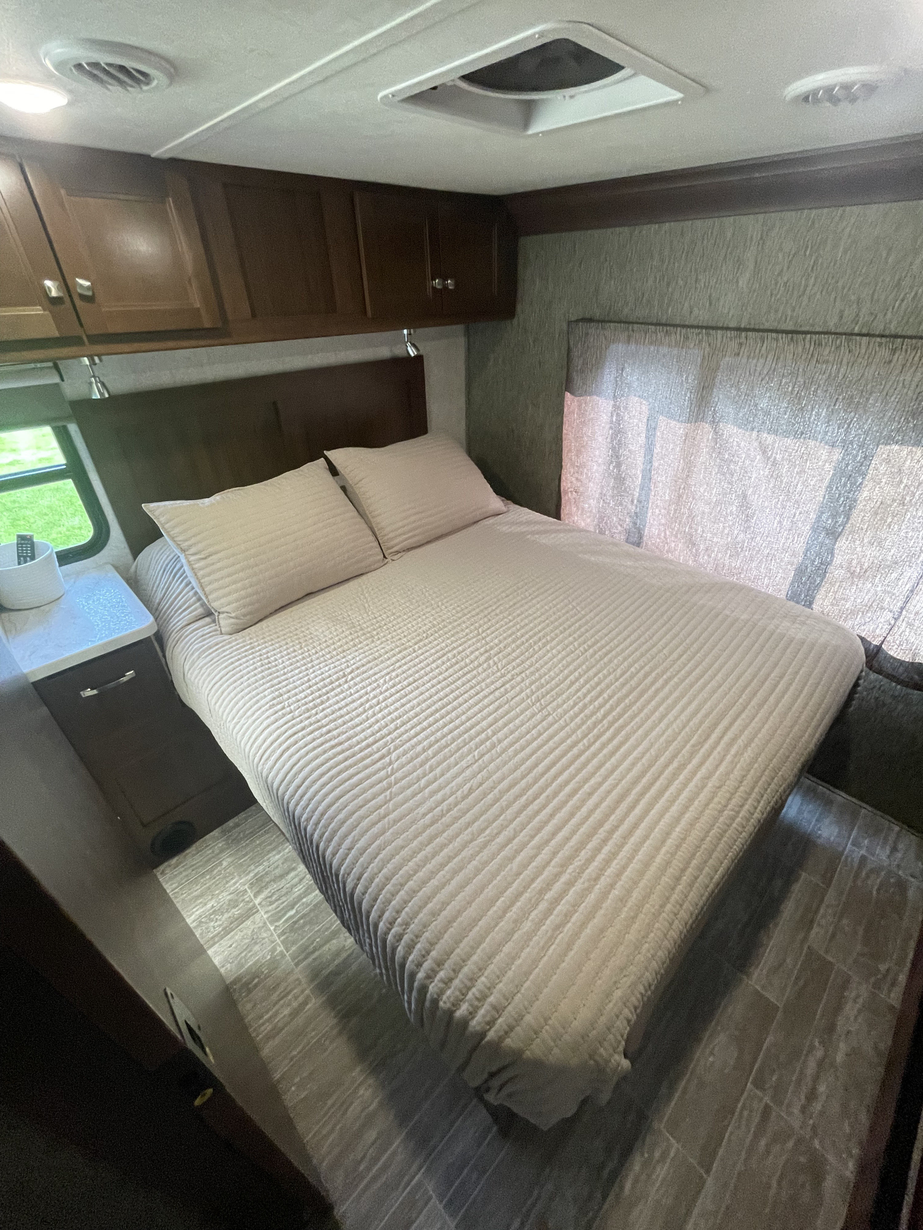 Cozy RV rental bedroom featuring a made bed, wall cabinets, ceiling vents, and a window.. Forester Forester Motorhome 2018