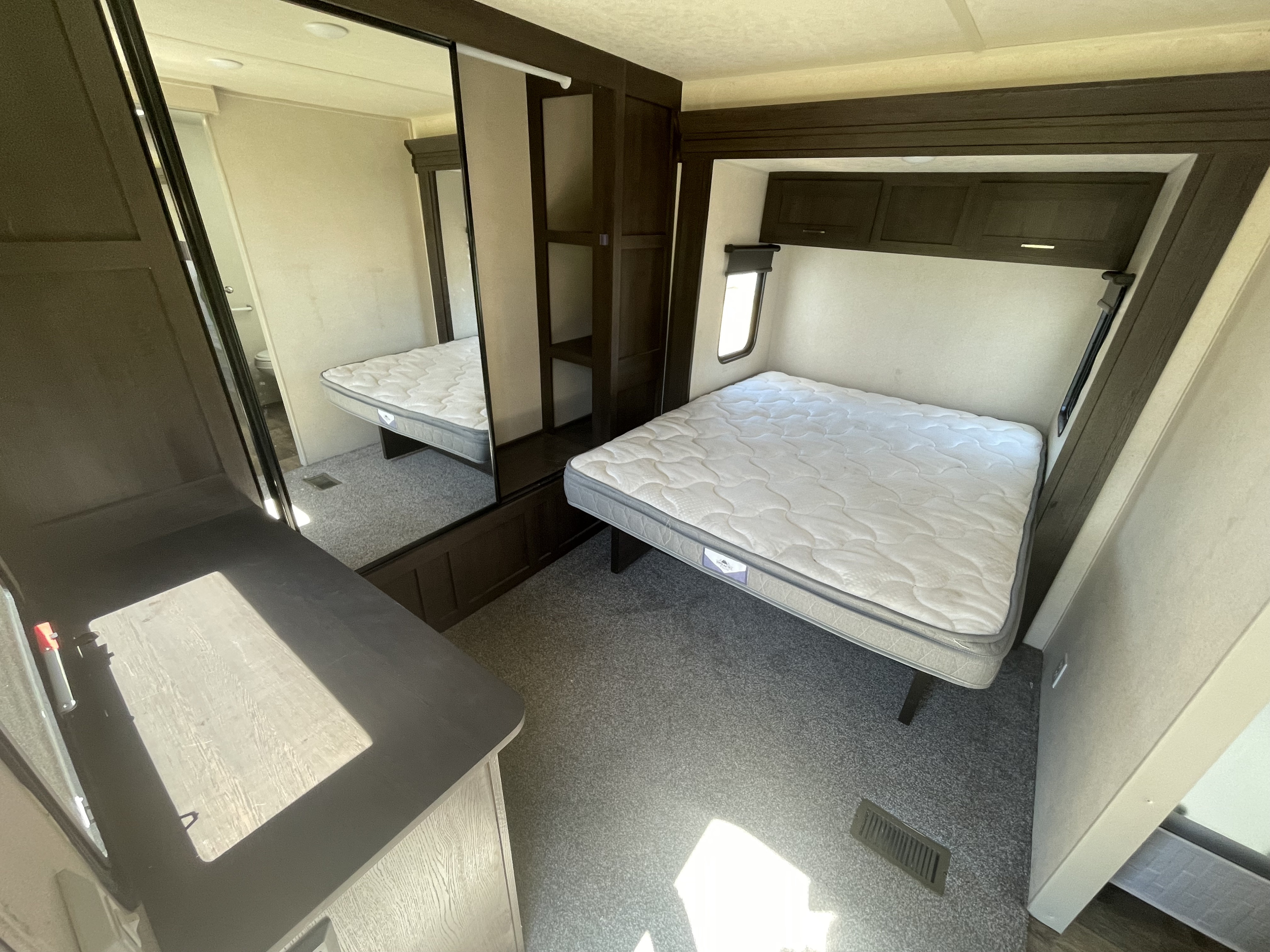 Inside this RV rental bedroom: a cozy bed, overhead storage, mirrored closet reflecting a bathroom, and plush carpeting.. Forest River Wildwood 2019