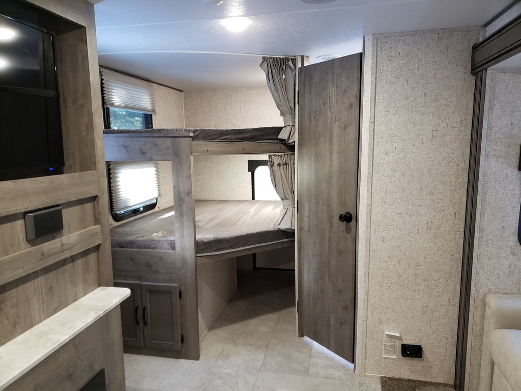 RV rental interior showcasing comfortable bunk beds, a TV entertainment unit, and a private door. Perfect for family travel.. Coachmen Apex 2020