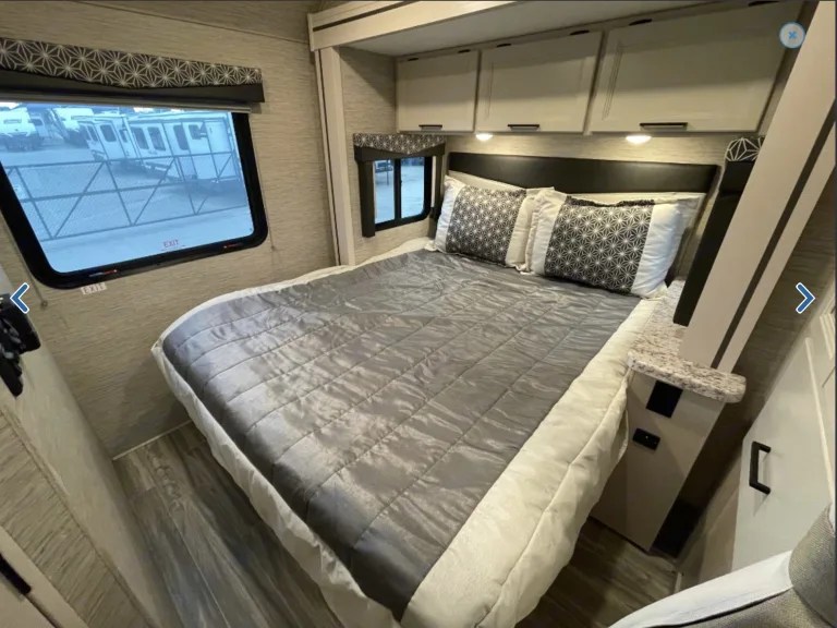 **RV rental** bedroom interior: A cozy bed with gray bedding, overhead cabinets, and a window view. Ideal for travel comfort.. Thor Freedom Elite 2023