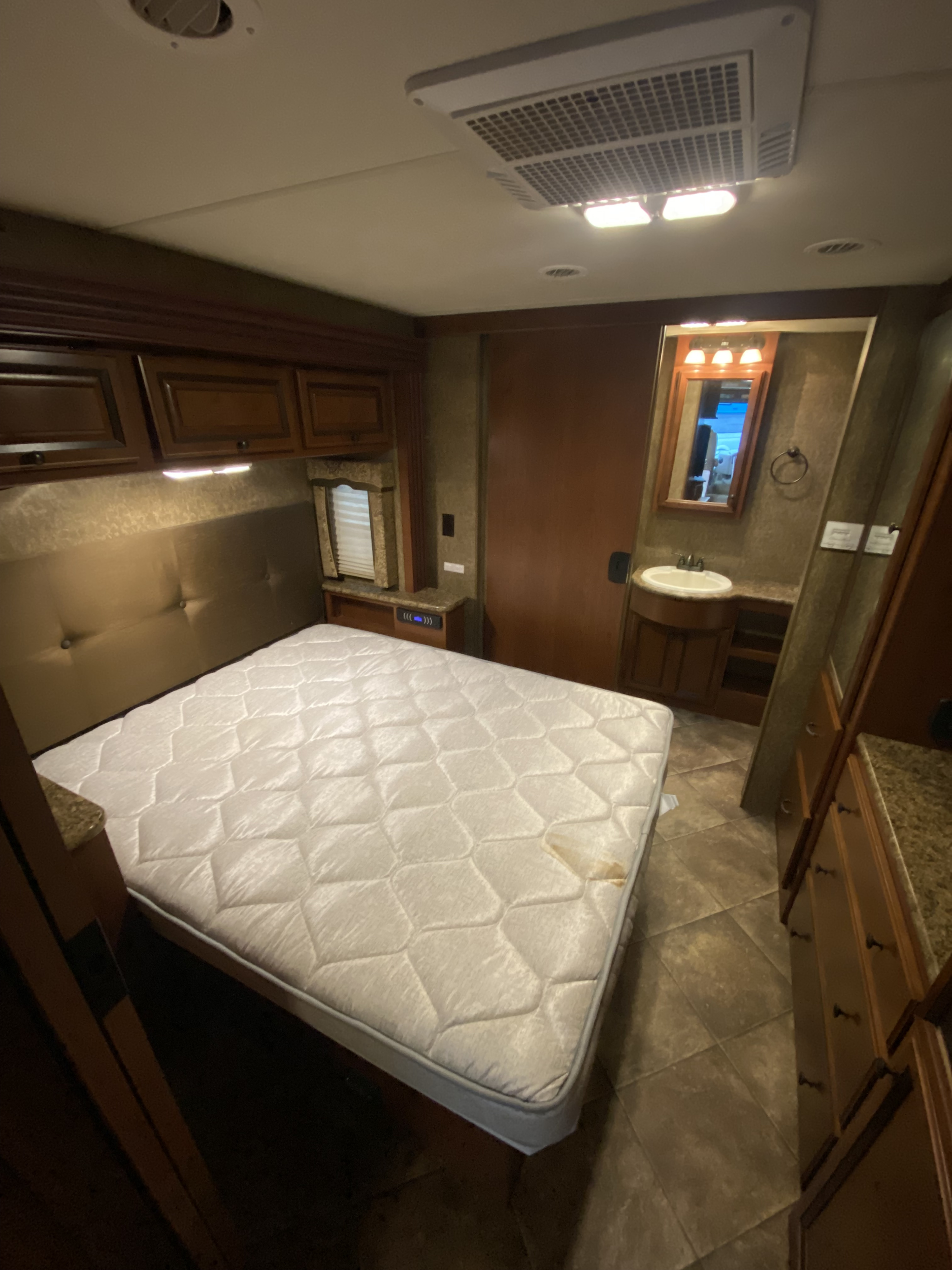 RV rental bedroom interior: stained mattress, overhead cabinets, AC unit, and compact adjacent bathroom.. Thor Windsport 2015