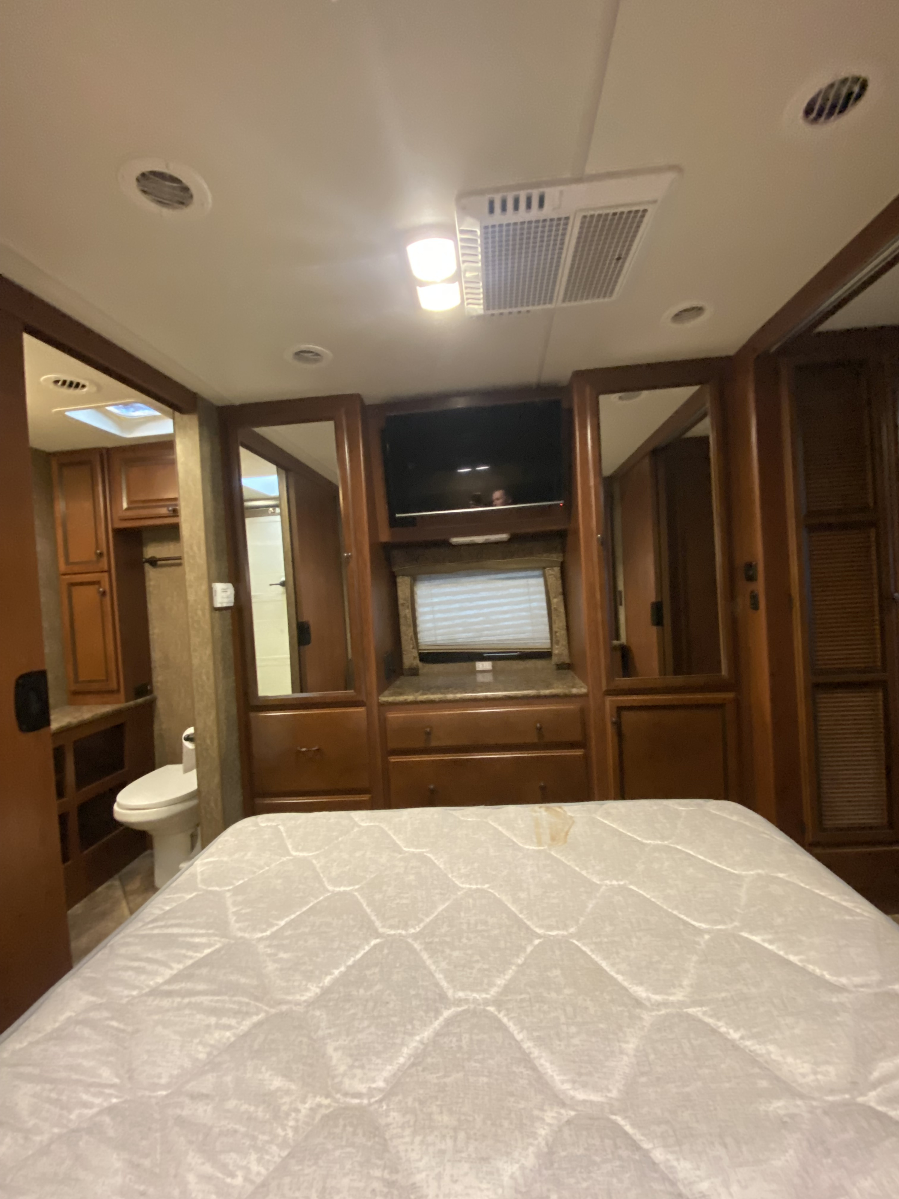 Spacious RV rental bedroom with TV, storage, and visible bathroom, featuring a quilted mattress in the foreground.. Thor Windsport 2015