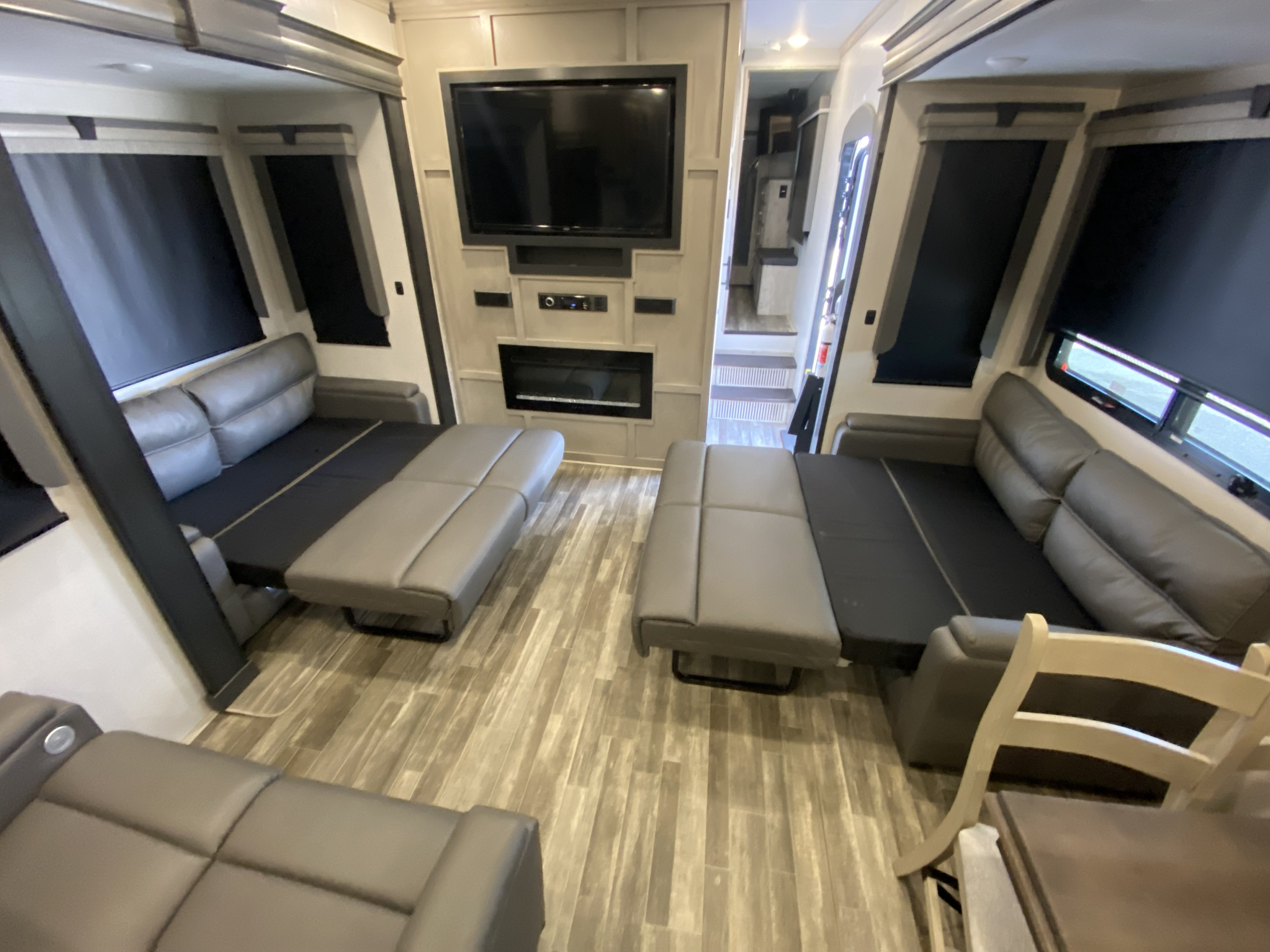 Spacious RV rental living area featuring gray sleeper sofas, entertainment center with TV & fireplace, and wood-look flooring.. Keystone RV Alpine 2022