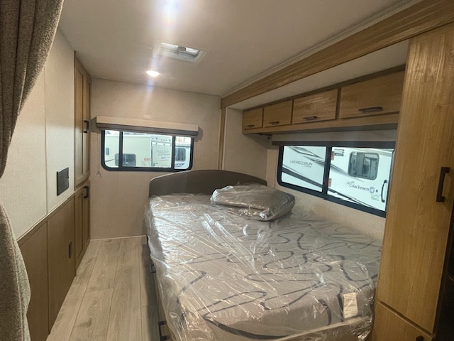 Discover a comfy RV rental bedroom interior: bed with protective cover, overhead storage, and bright windows.. Coachmen Leprechaun 2025