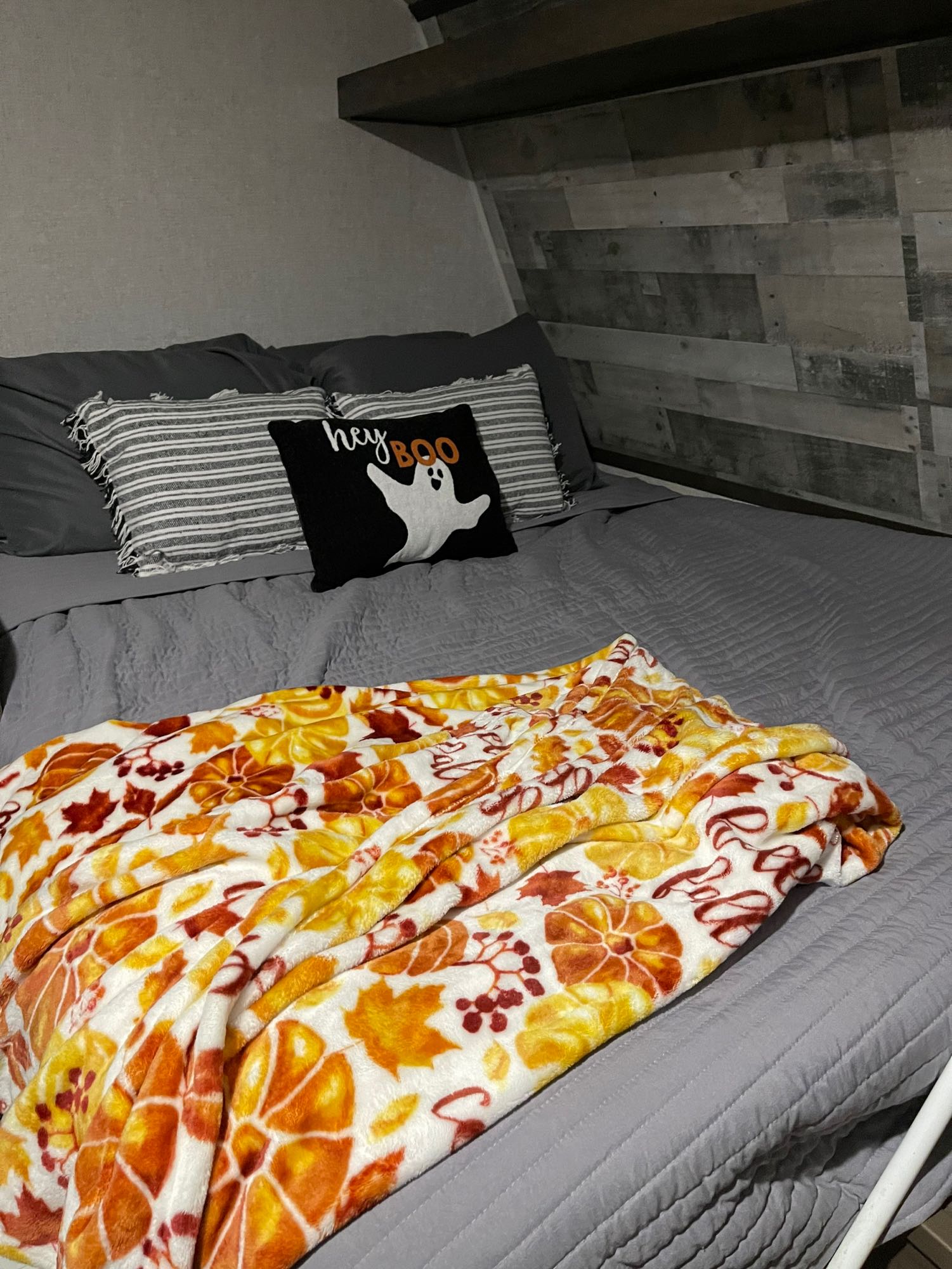 Inside an rv rental, a cozy bed features gray linens, a "hey boo" ghost pillow, and a fall-themed blanket.. Dutchmen Coleman Lantern LT 2022