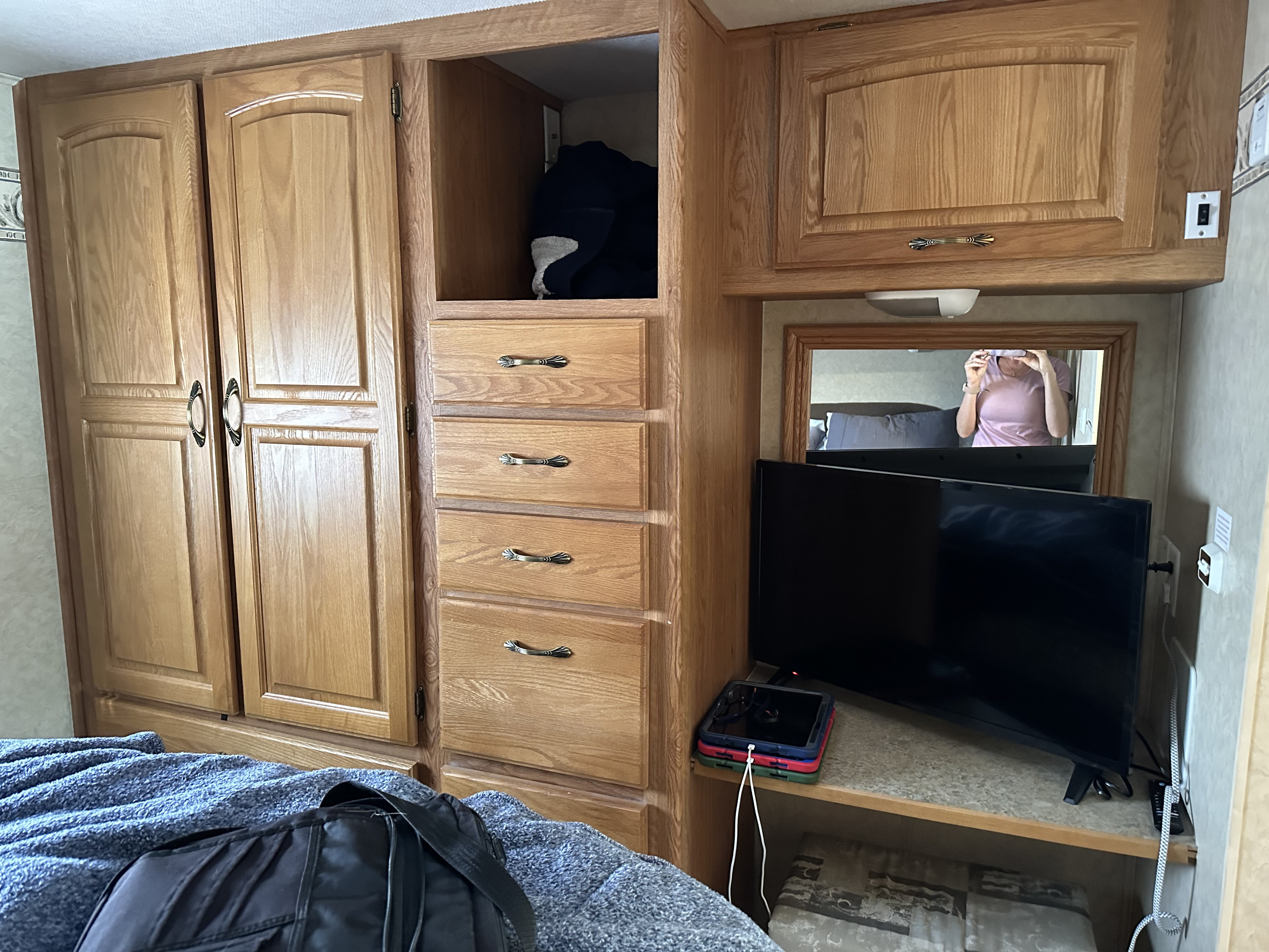 RV rental bedroom interior featuring wood cabinets, drawers, TV, and a mirror, offering compact storage and amenities.. Jayco Greyhawk 2006