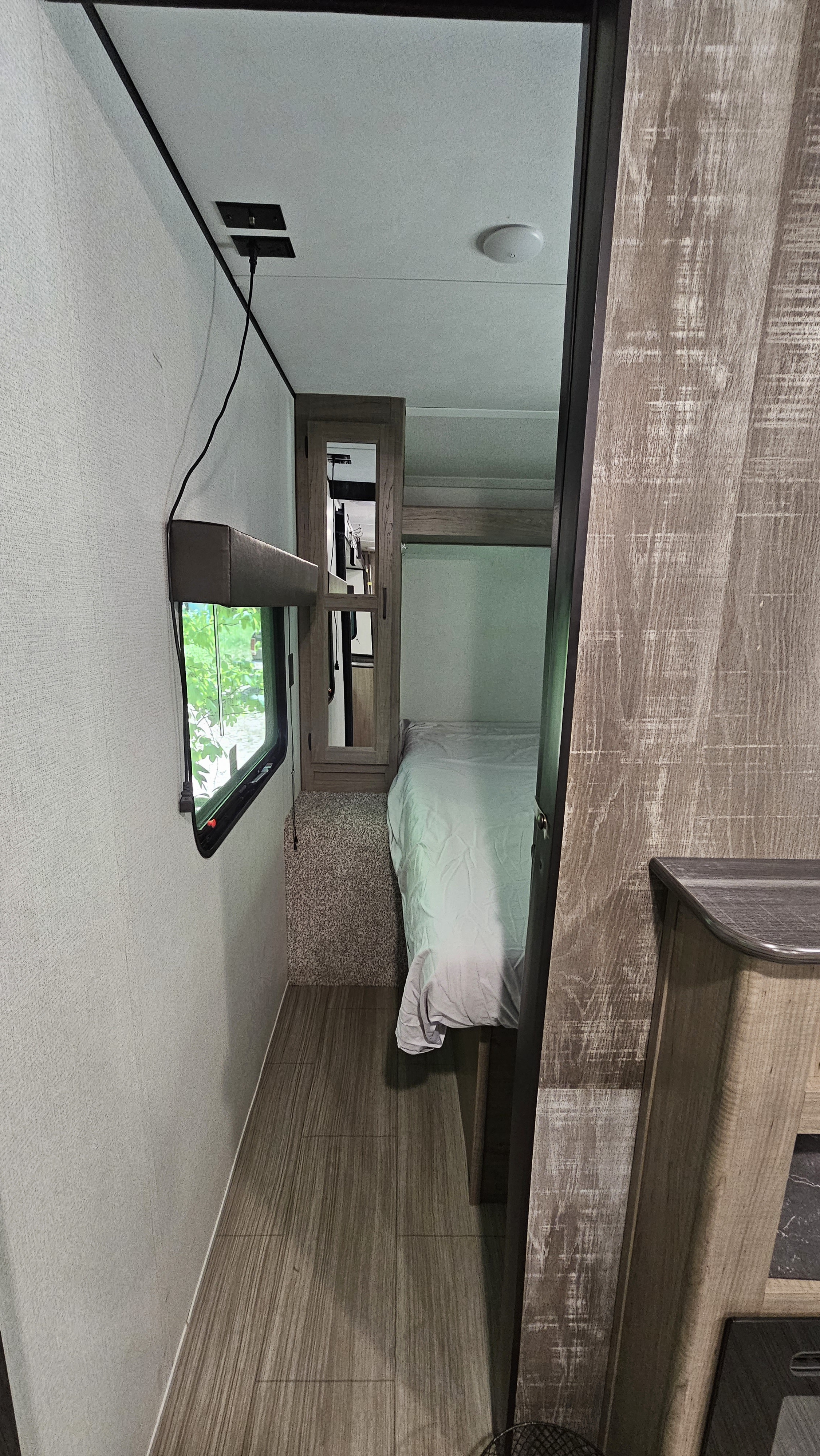 RV rental interior view of a compact hallway leading to a bright bedroom with a bed and window, perfect for travel.. Keystone Hideout 2021