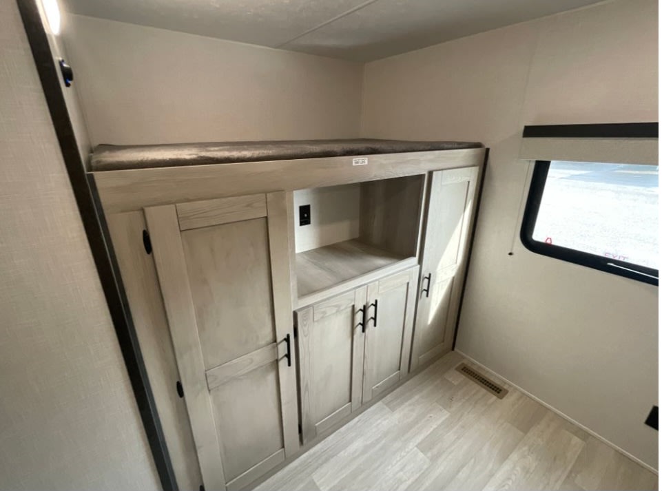 RV rental bunk bed & storage cabinets. This RV interior features a top bunk, light wood cabinetry, and window.. KZ C312BHKSE 2022