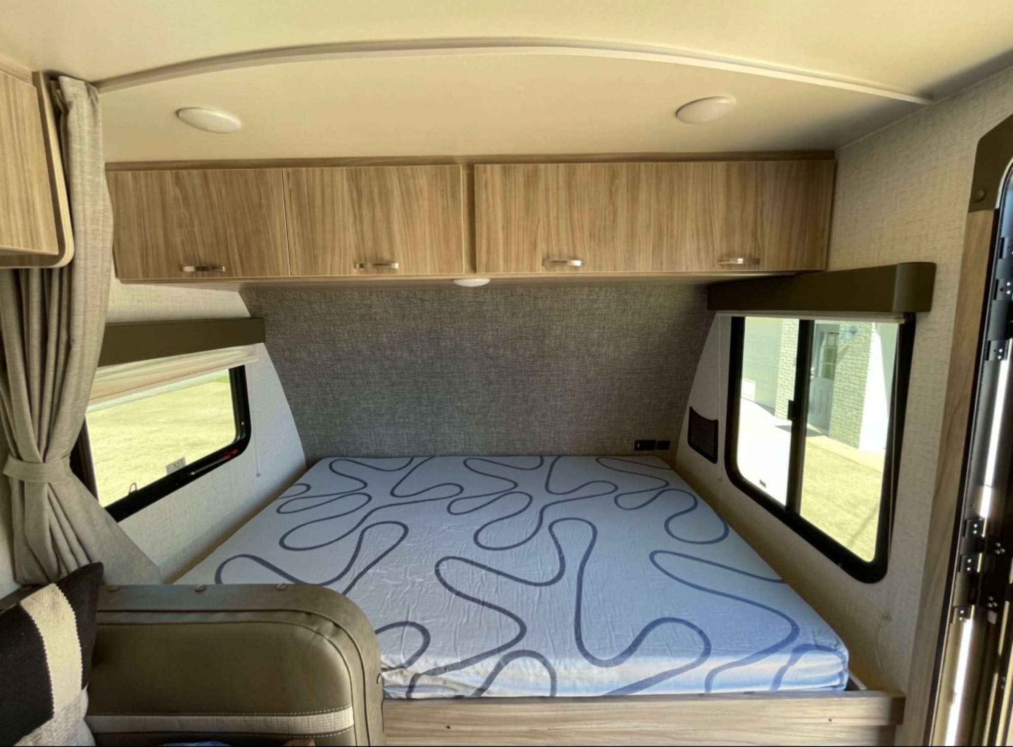 Cozy RV rental bedroom featuring a patterned bed, light wood overhead cabinets, and two side windows for natural light.. Minnie Micro Minnie 2022