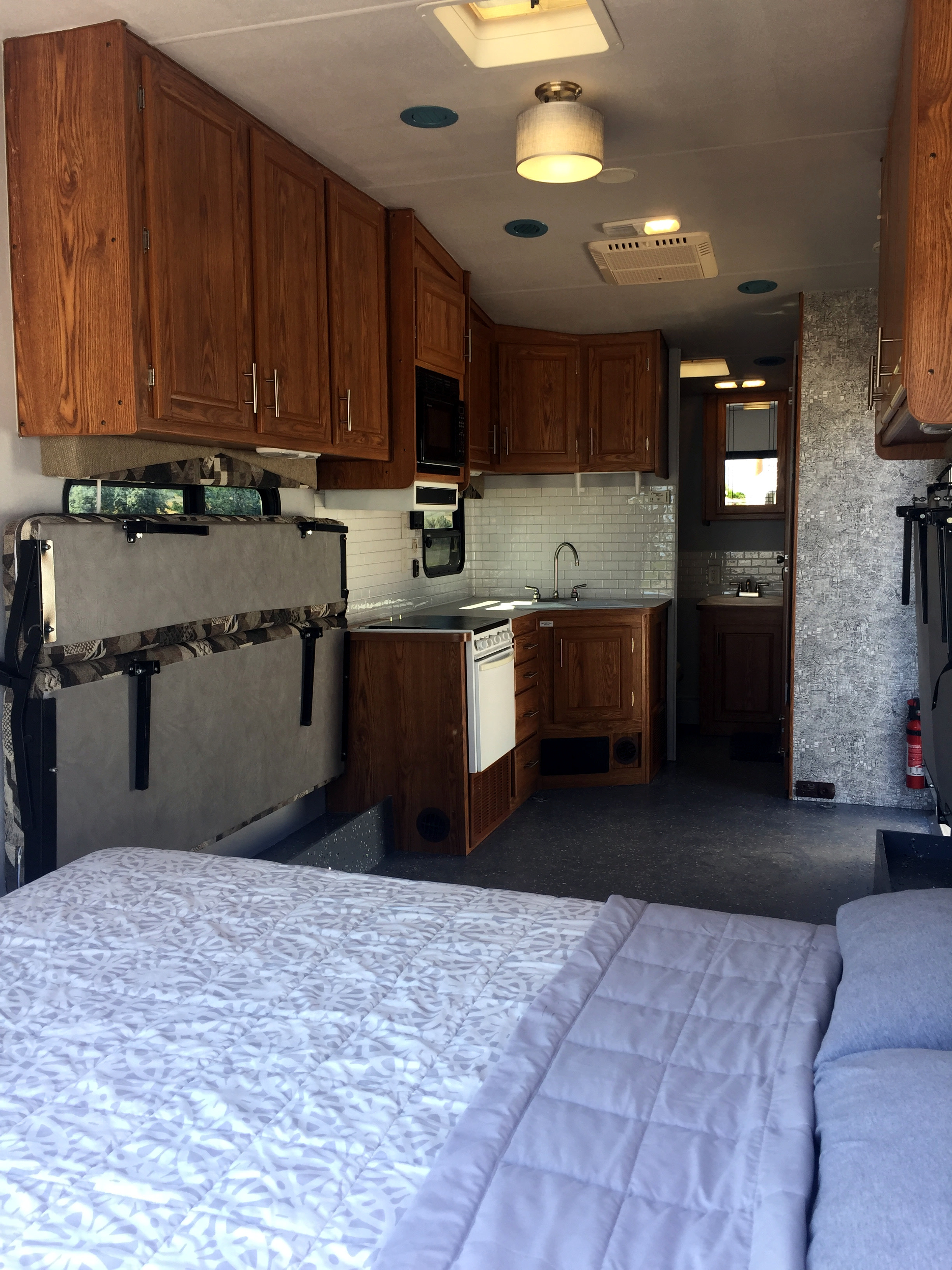 Bright RV rental interior featuring a compact kitchen with wood cabinets, sink, and stove, plus a bed and foldable bunk.. Northwood Mfg Desert Fox 2003
