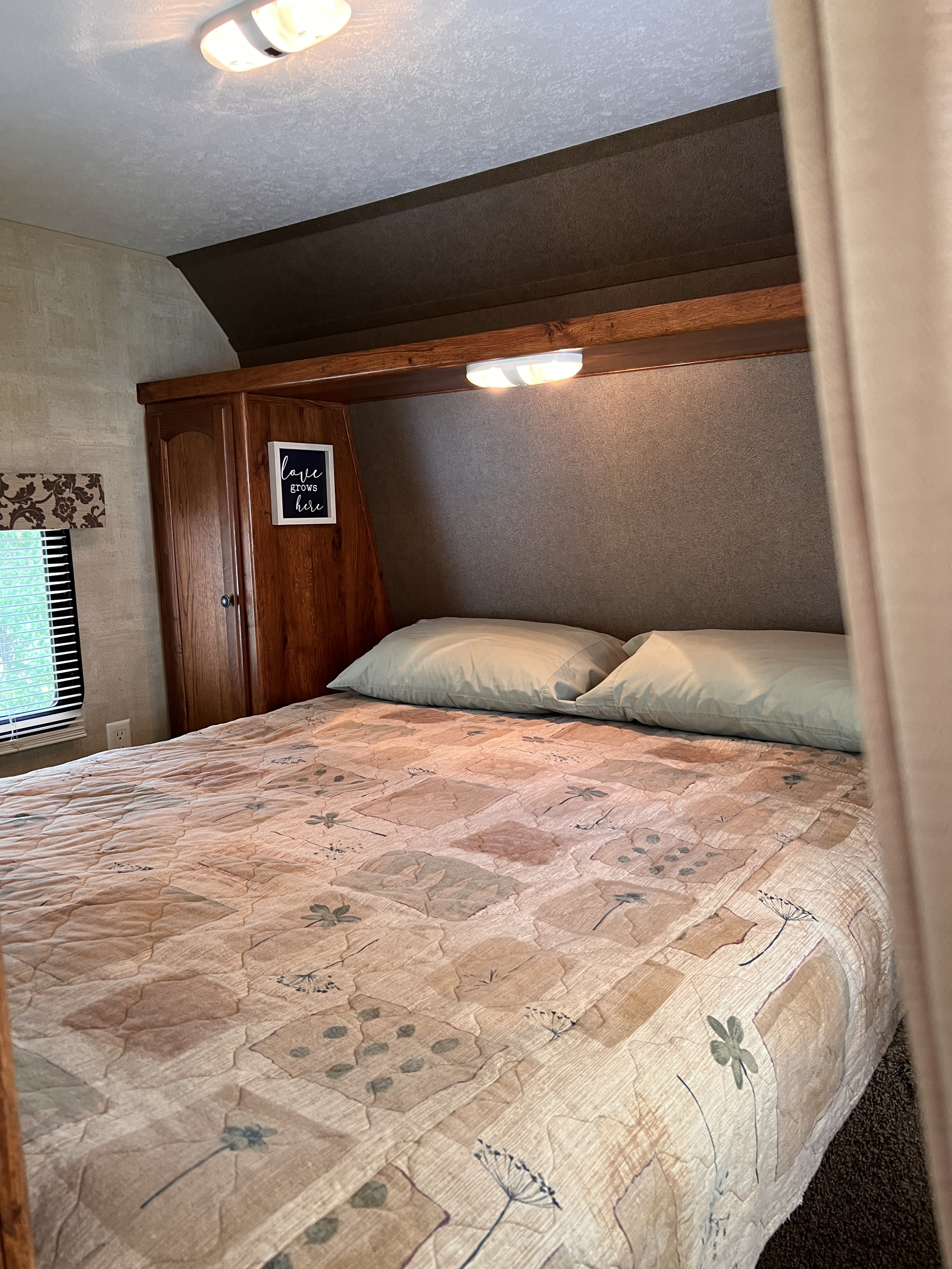 Inside a cozy RV rental: a bedroom with a patterned comforter, wood cabinetry headboard, and a "love grows here" sign.. Keystone Hideout LHS 2014