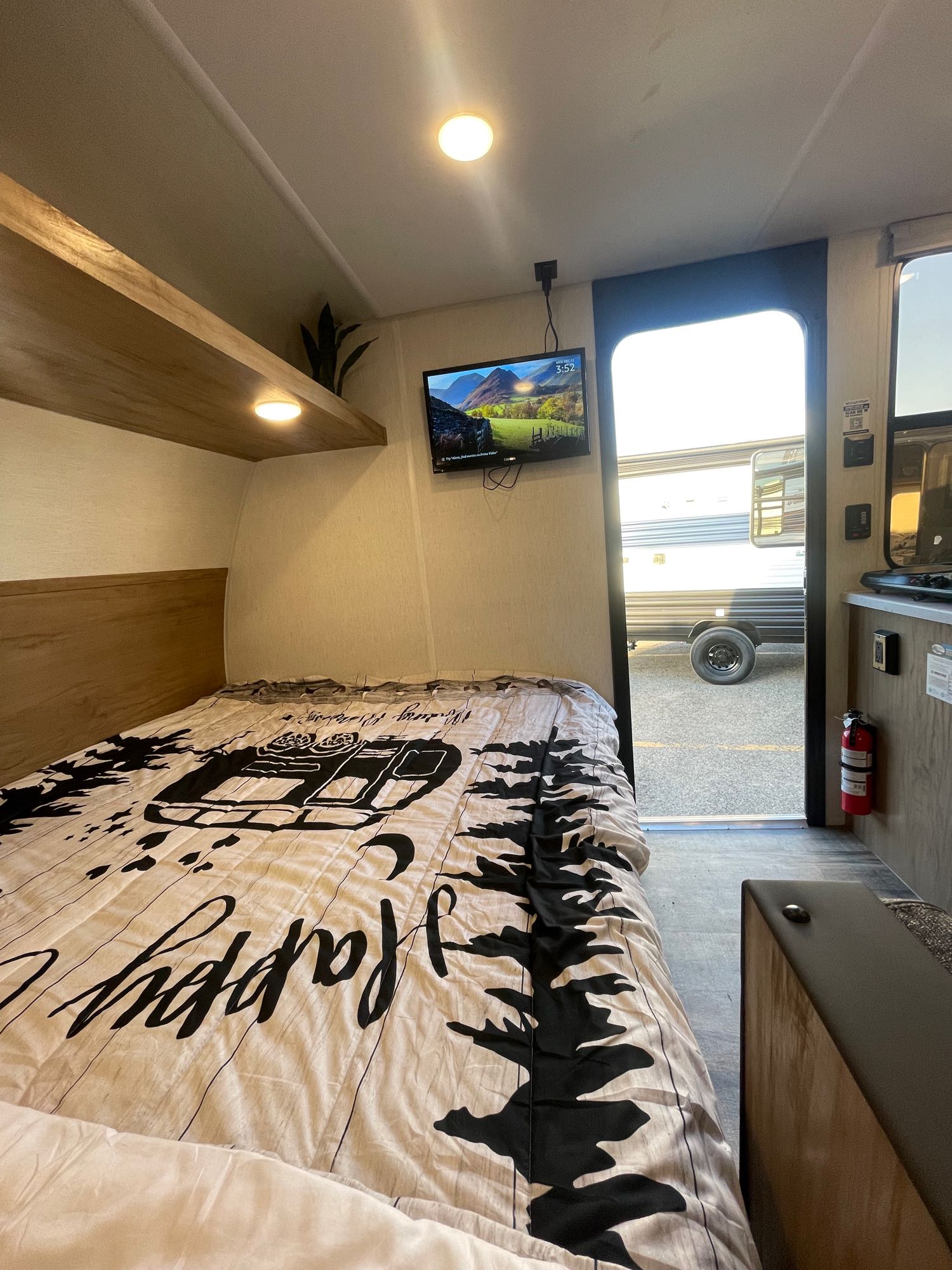 Step inside this cozy RV rental bedroom: a comfy bed with "Happy Camper" duvet, TV, and an open door to the outside.. Forest River Wolf Den 16EV 2024