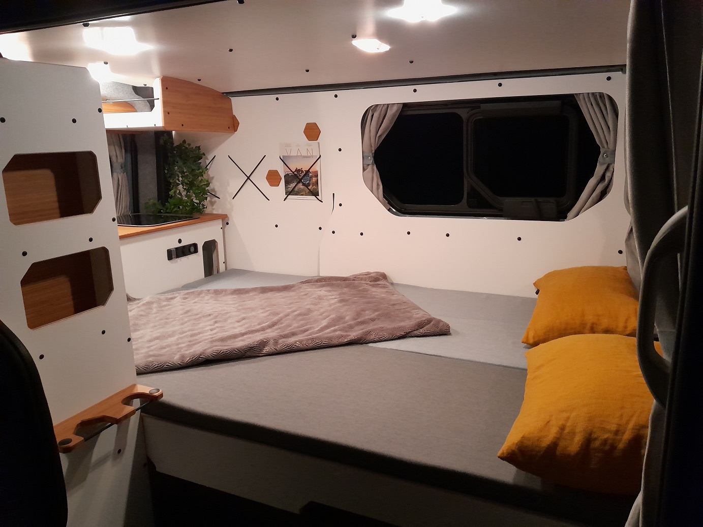 Modern camper van RV rental interior featuring a bed with orange pillows, storage, and cozy lighting.. Renault Trafic 3 - année 2024 2024