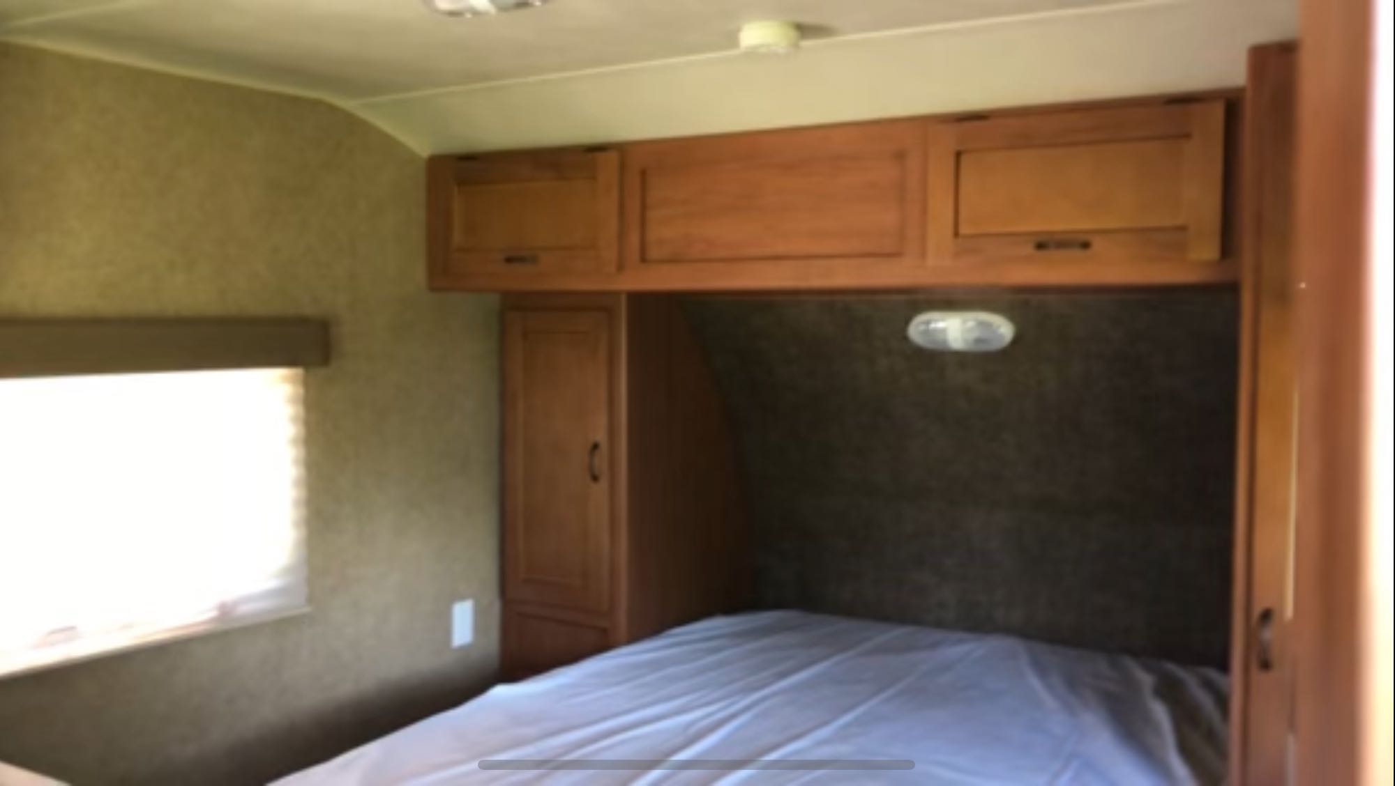 Interior of an RV rental bedroom showing a bed, overhead cabinets, a wardrobe, and a window with blinds.. Forest River Cherokee Grey Wolf 2013