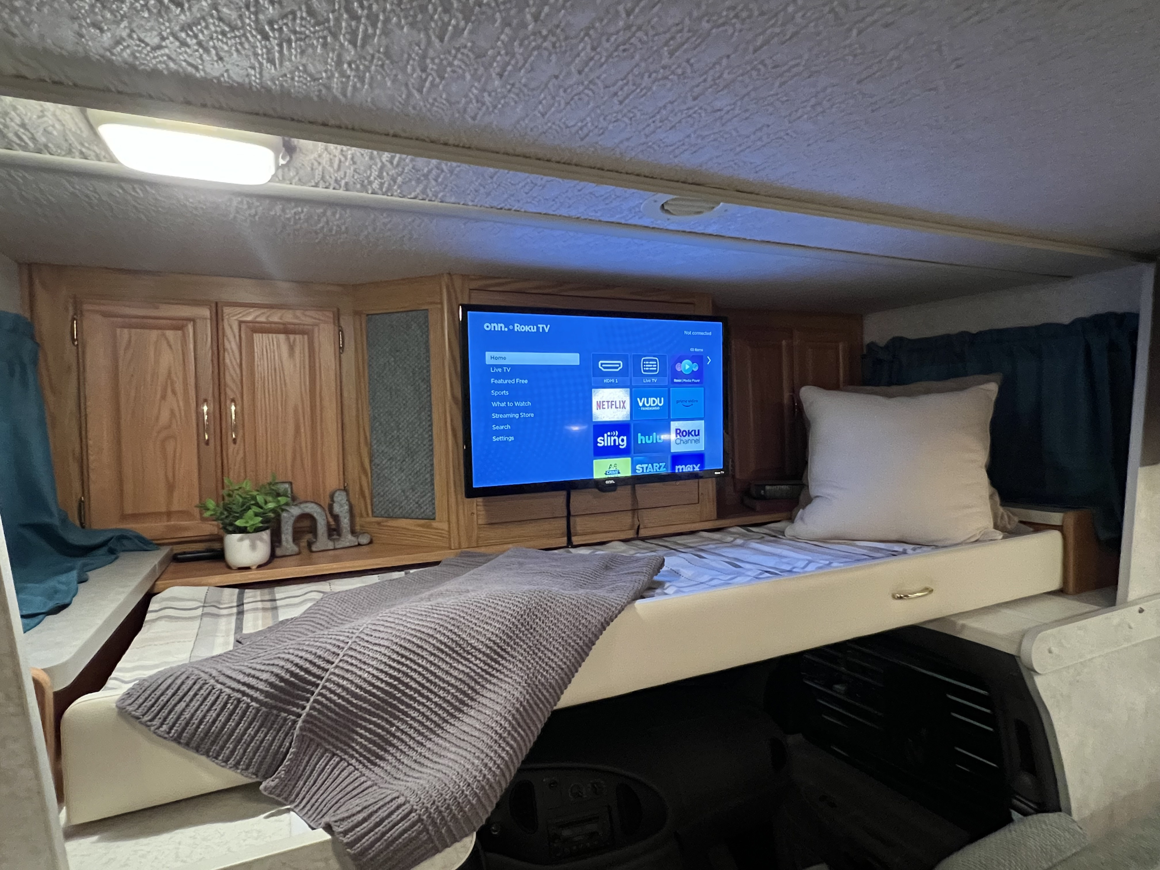 Cozy RV rental interior: a bunk bed with a gray blanket, Roku TV with streaming apps, and wood cabinets. Perfect for trips!. Winnebago Minnie 2002