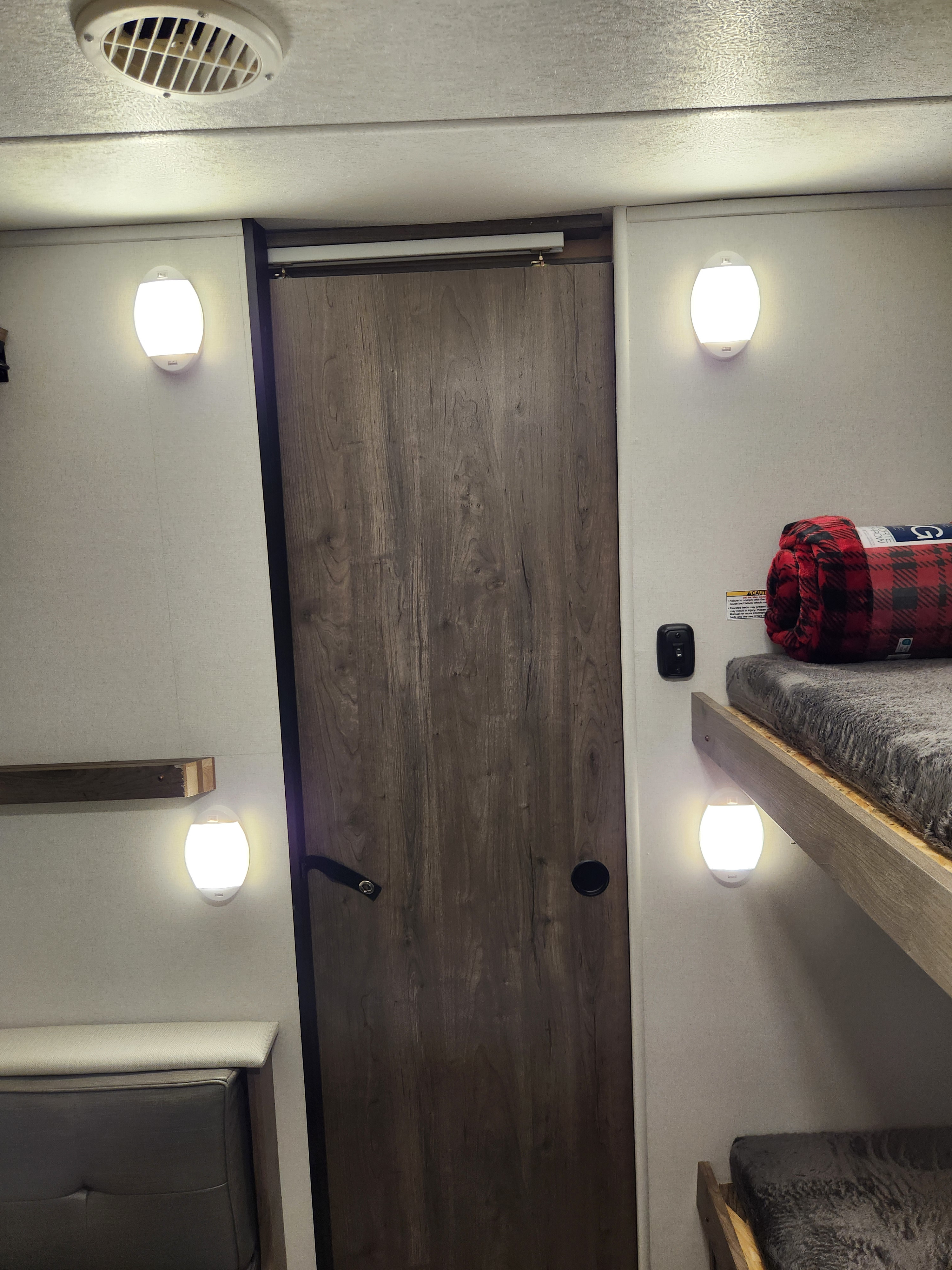 This RV rental shows bunk beds on the right, a central door, and a sofa/shelf on the left, lit by bright LED lights.. Heartland RVs Pioneer 2024
