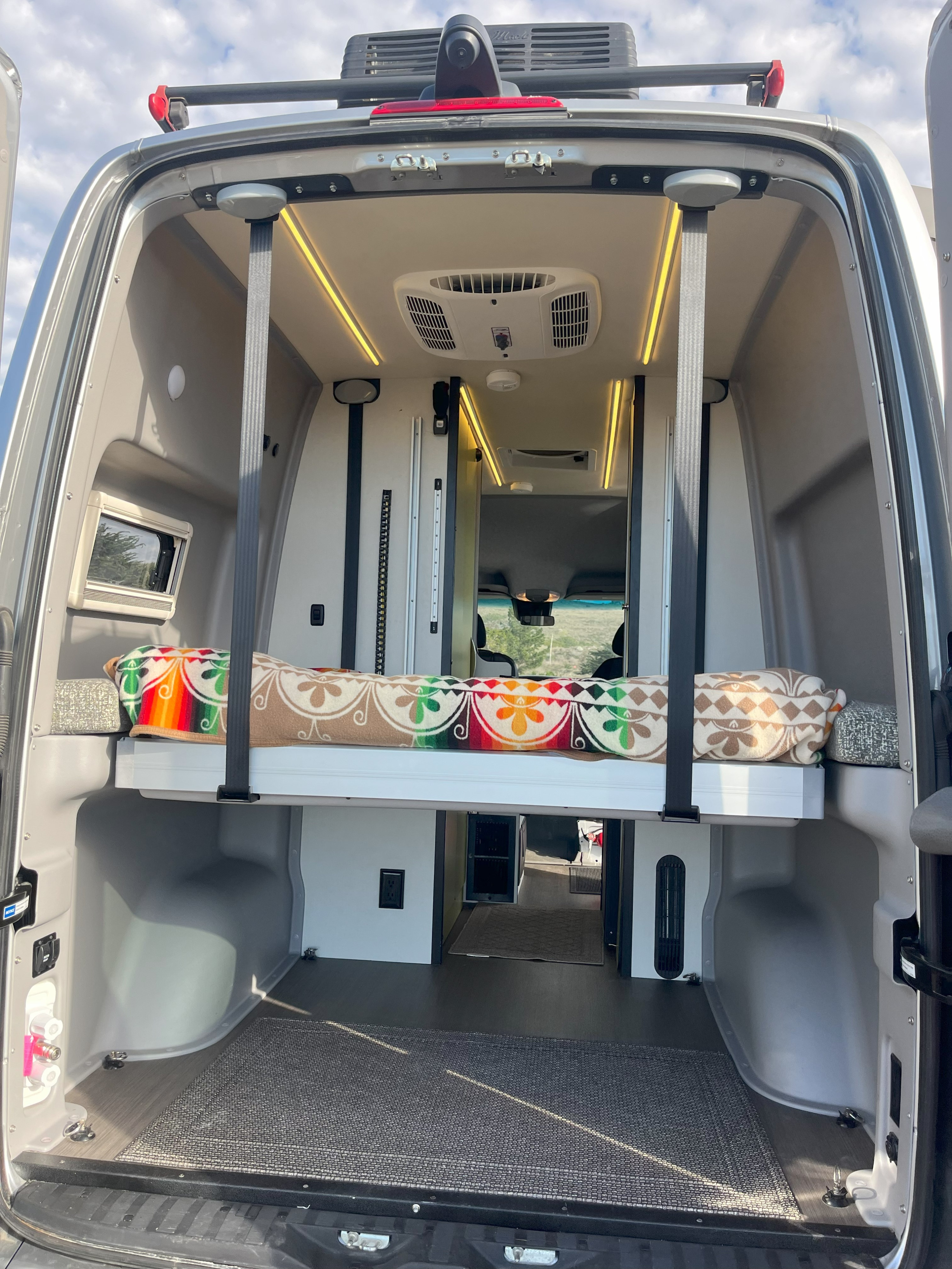 Inside a modern rv rental camper van, revealing a raised bed, ceiling AC, and warm strip lighting.. Winnebago Revel 2019