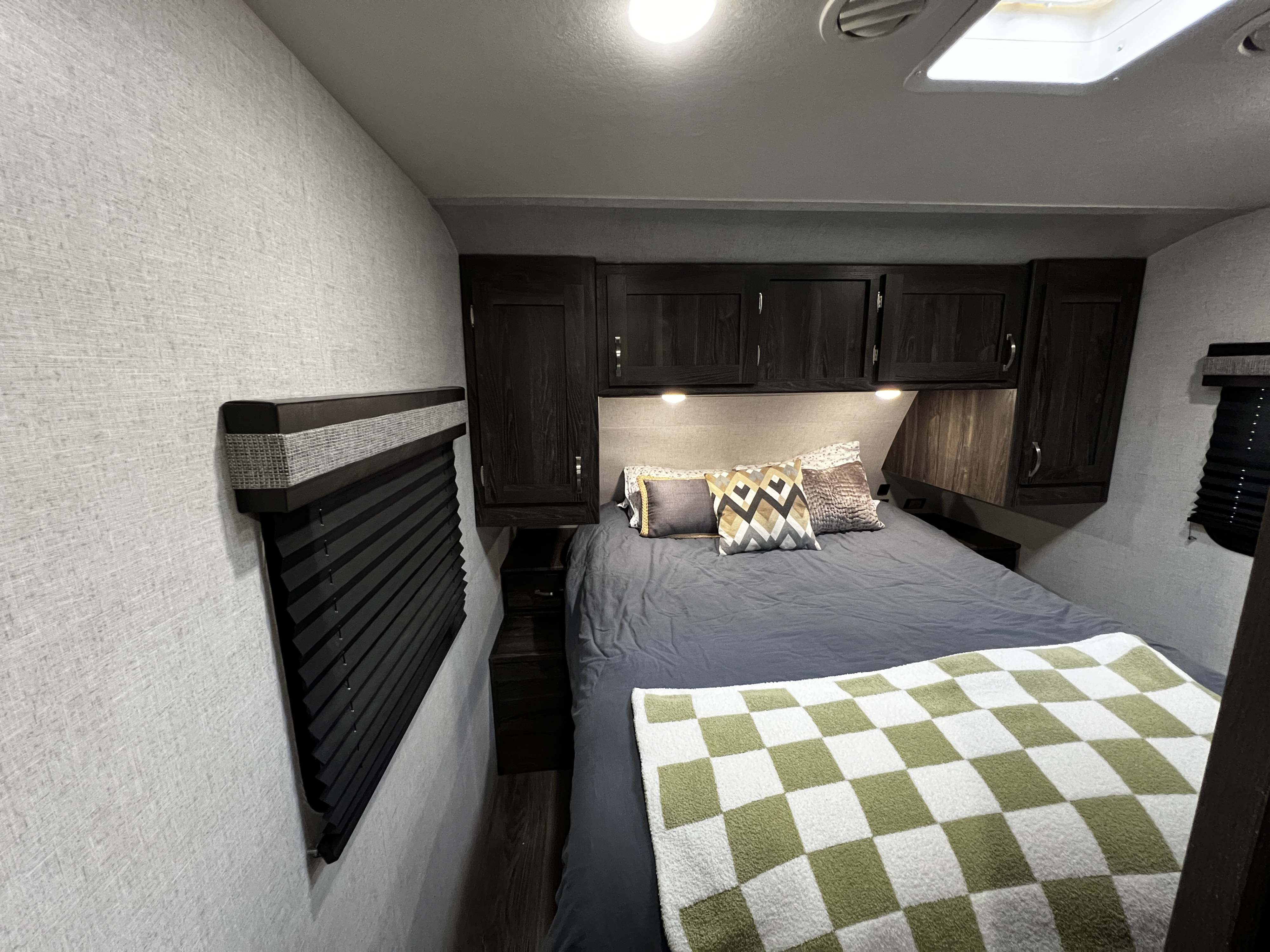 A cozy RV rental bedroom interior features a comfy bed with decorative pillows, dark overhead cabinets, and window blinds.. Highland Ridge RV Mesa Ridge Lite 2020