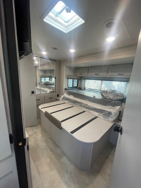 Bright RV rental bedroom: large skylight, unmade bed platform, overhead cabinets, and mirrored closet enhance space.. Coachmen Freelander 2025