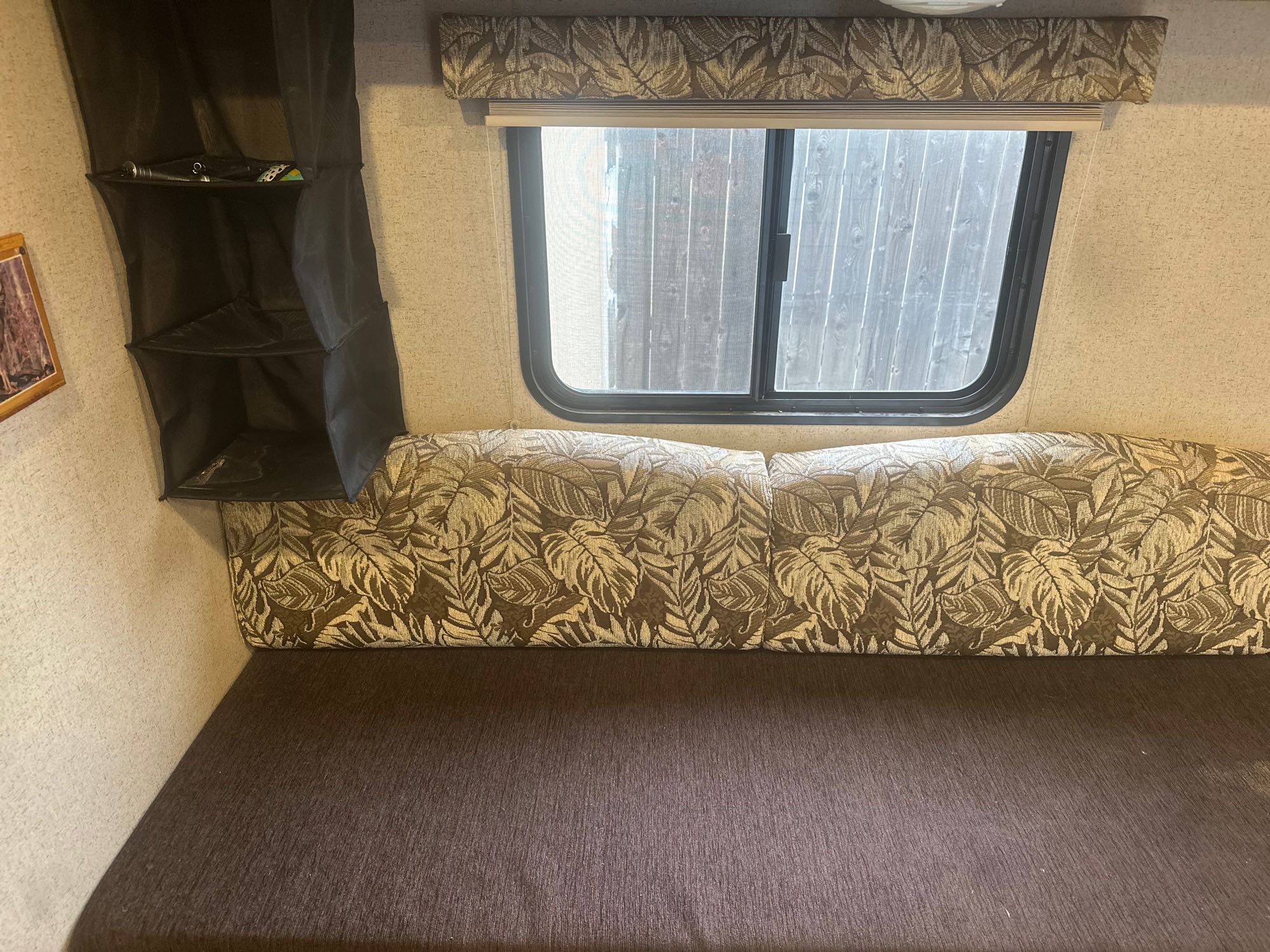 Inside an RV rental: a comfy sofa/bed with tropical leaf cushions, window, and hanging storage organizer.. Jayco Jay Flight SLX 2015